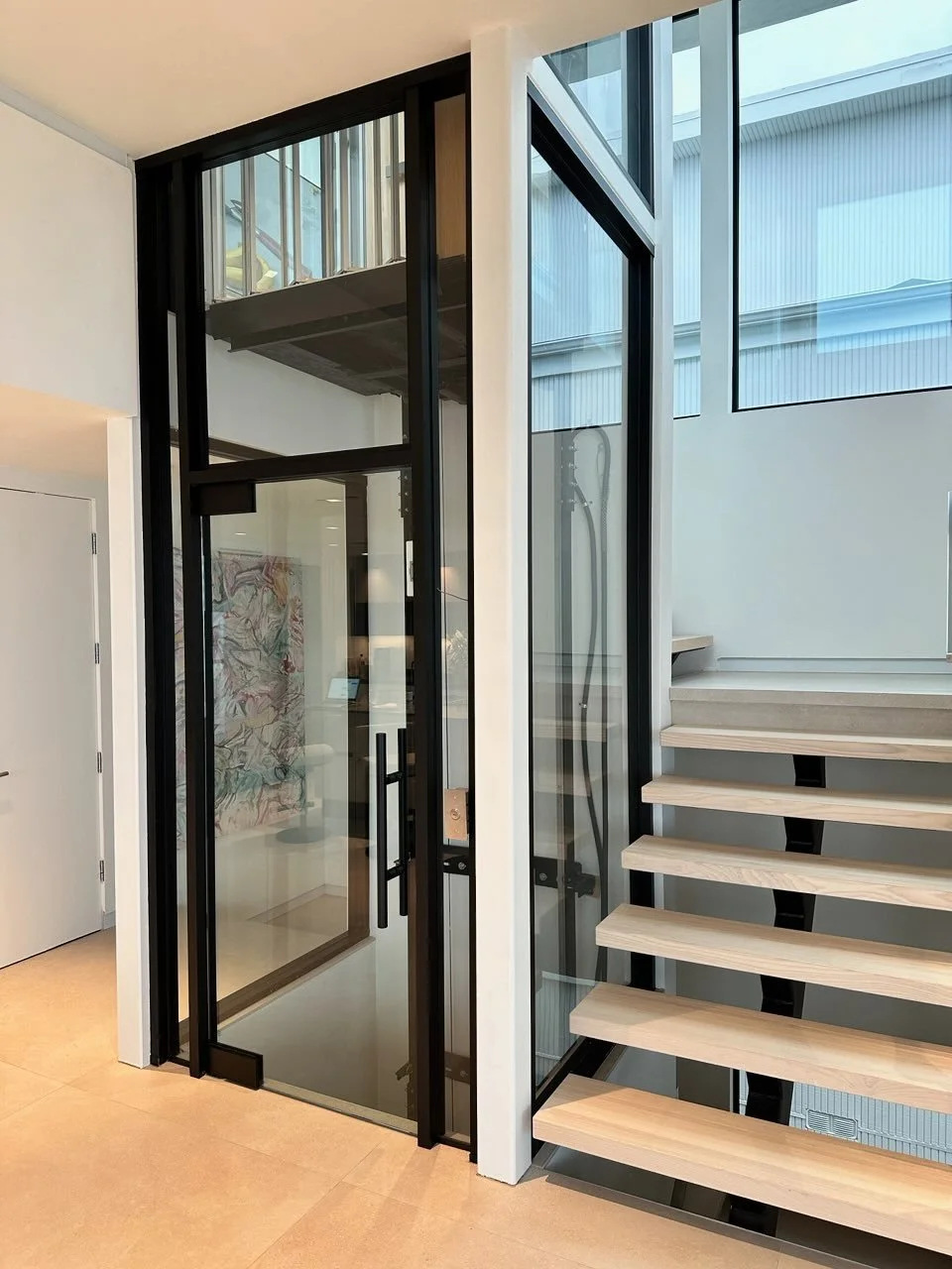 Interior view of a modern lobby with a glass elevator and staircase.
