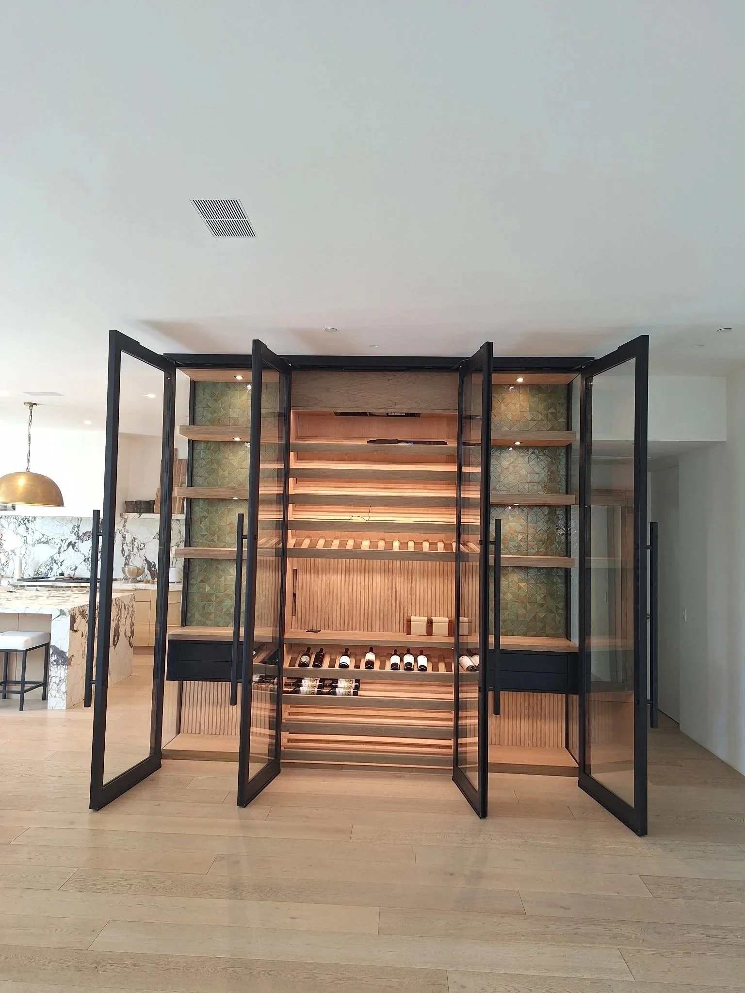 Modern wine storage cabinet with glass doors, wooden shelves, and wine bottles inside, situated in a home interior with a wooden floor.