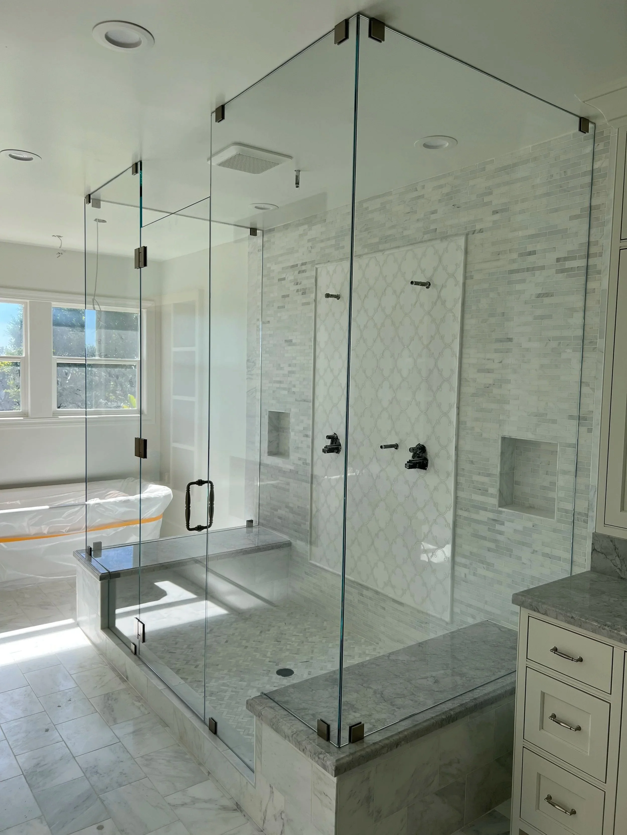 Modern bathroom with a glass shower enclosure, marble countertops, and a window with natural light.