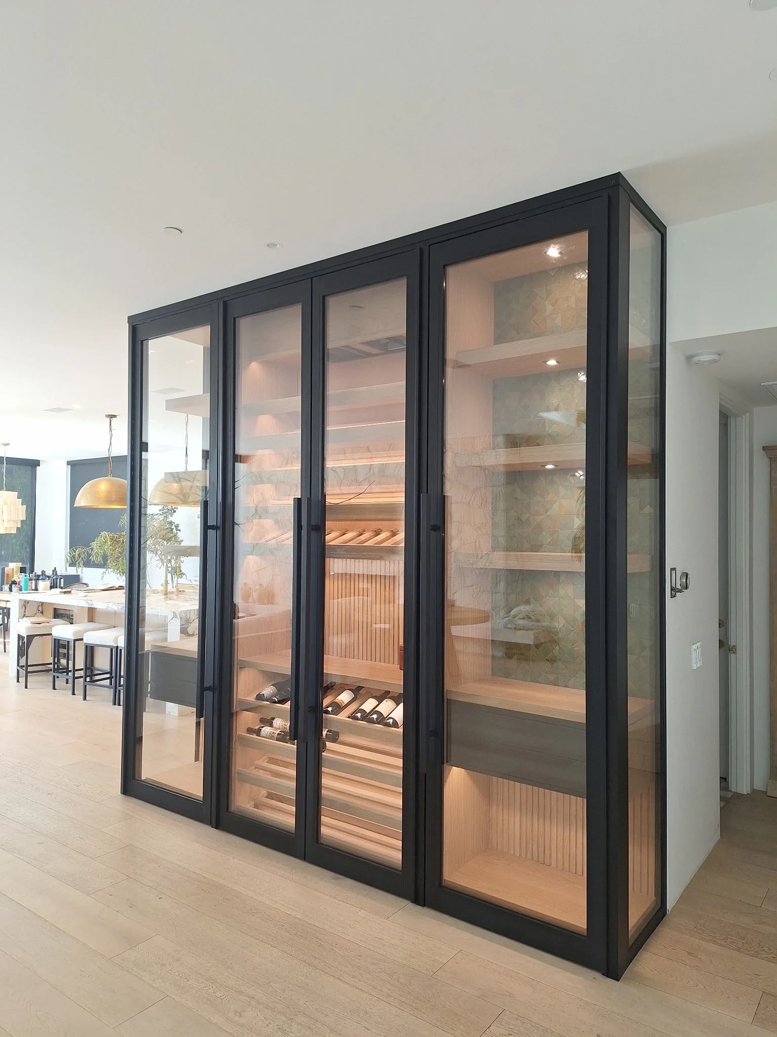 A modern wine storage cabinet with glass doors, wood interior shelves, and wine bottles inside, located in a contemporary open-plan living space.