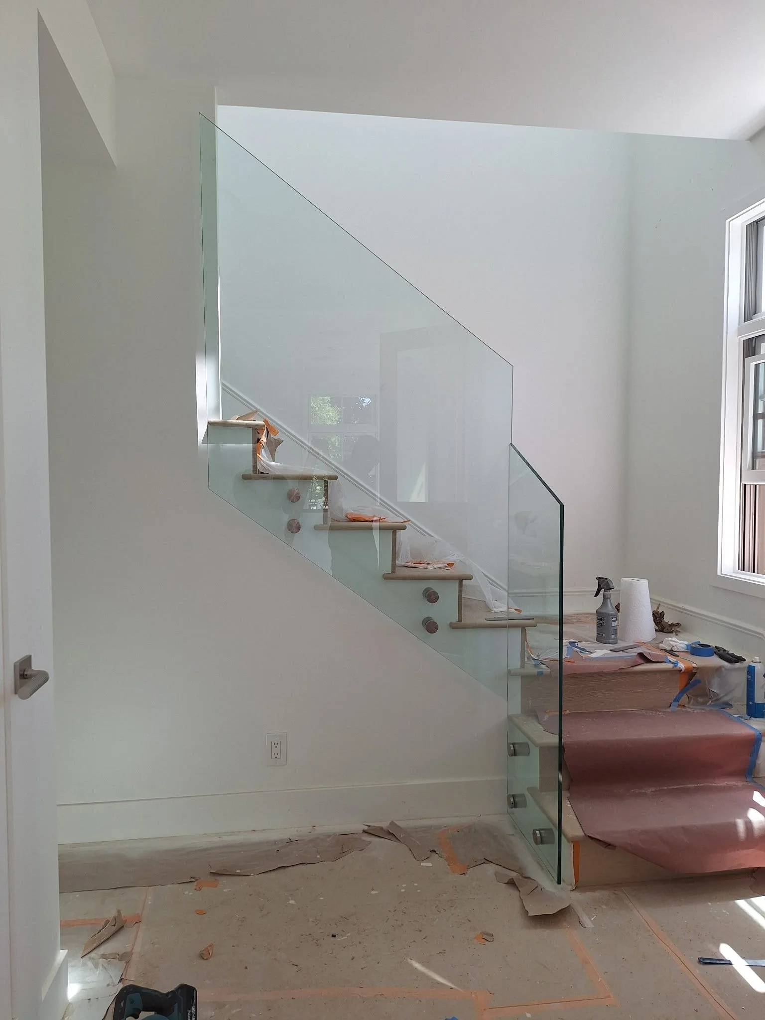 Interior of a house under construction with a glass staircase and a large window.