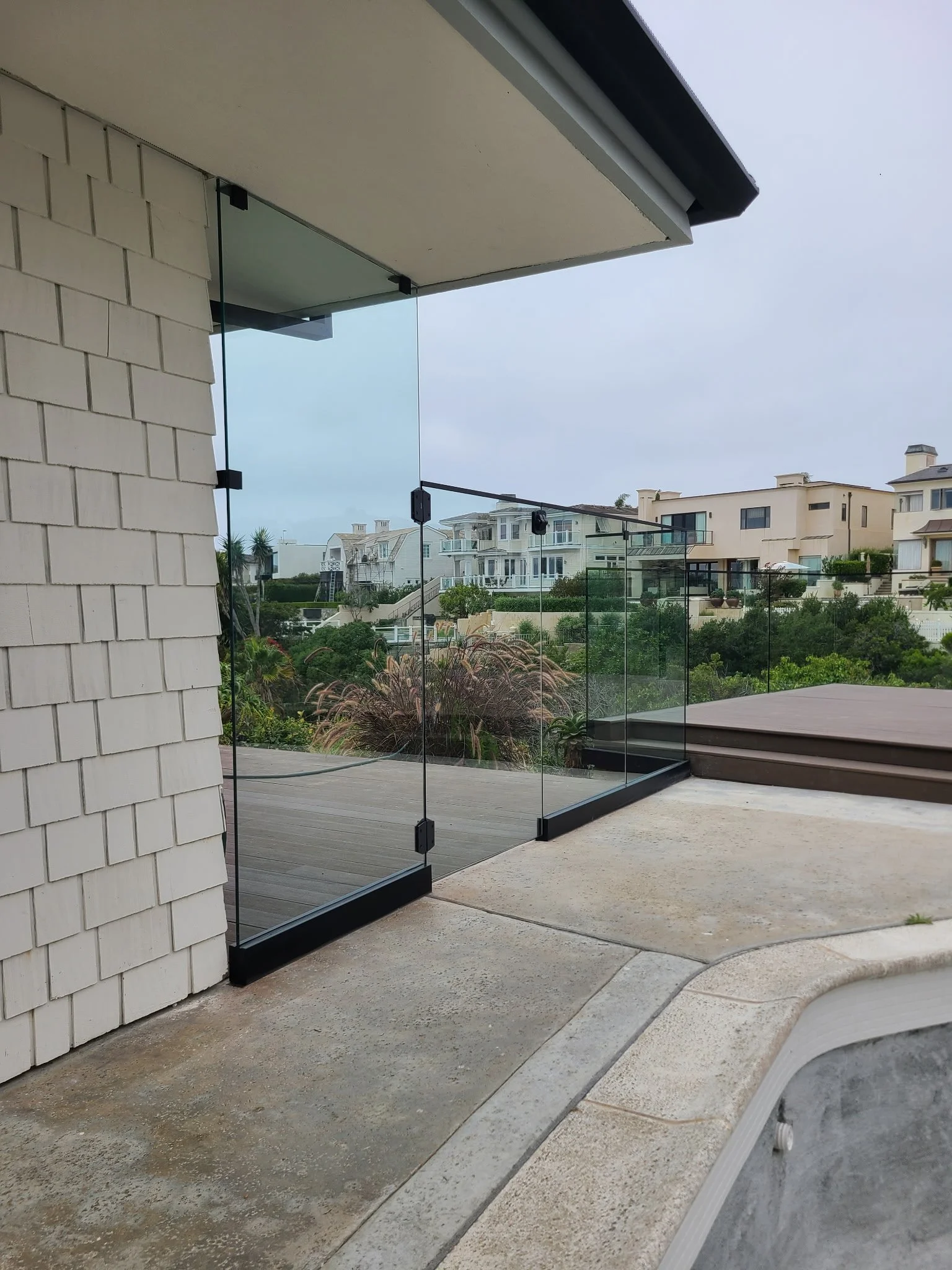 Modern balcony with glass railing overlooking residential neighborhood with white houses and greenery.