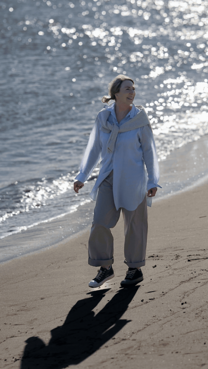 A woman walking along a beach shoreline on a sunny day.