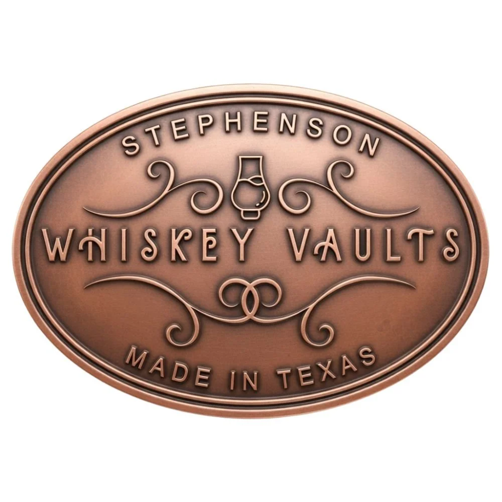 A copper-colored oval plaque with embossed text advertising Stephenson's Whiskey Vaults, made in Texas, featuring decorative swirls and a whiskey bottle illustration in the center.