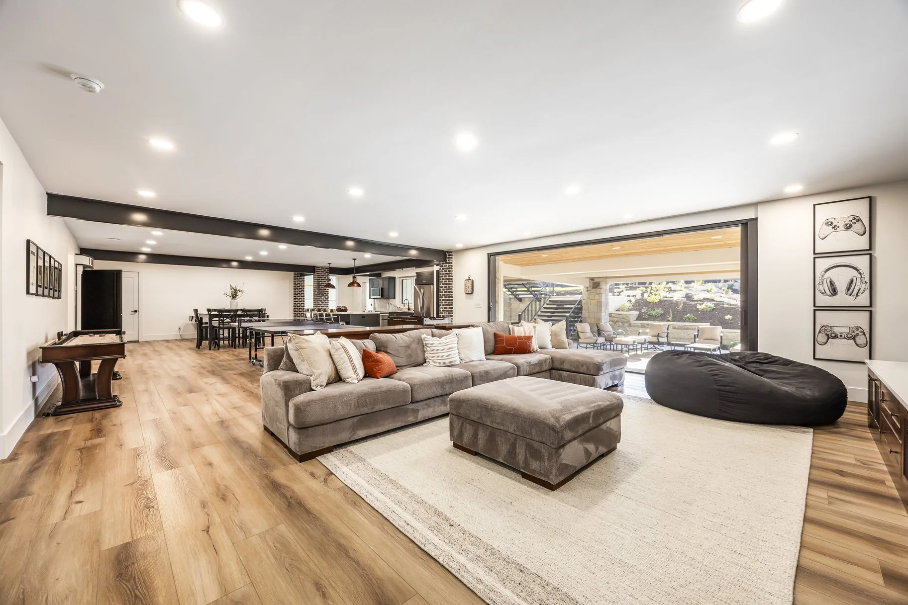 Spacious open-concept living room with beige sectional sofa, a large windowed wall, and wooden flooring.