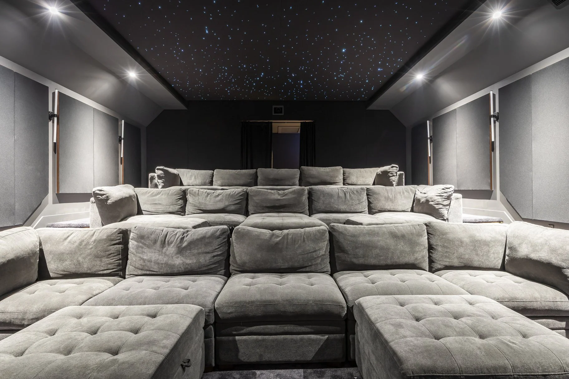A luxurious home theater with gray sectional sofas and a ceiling starry sky projection.