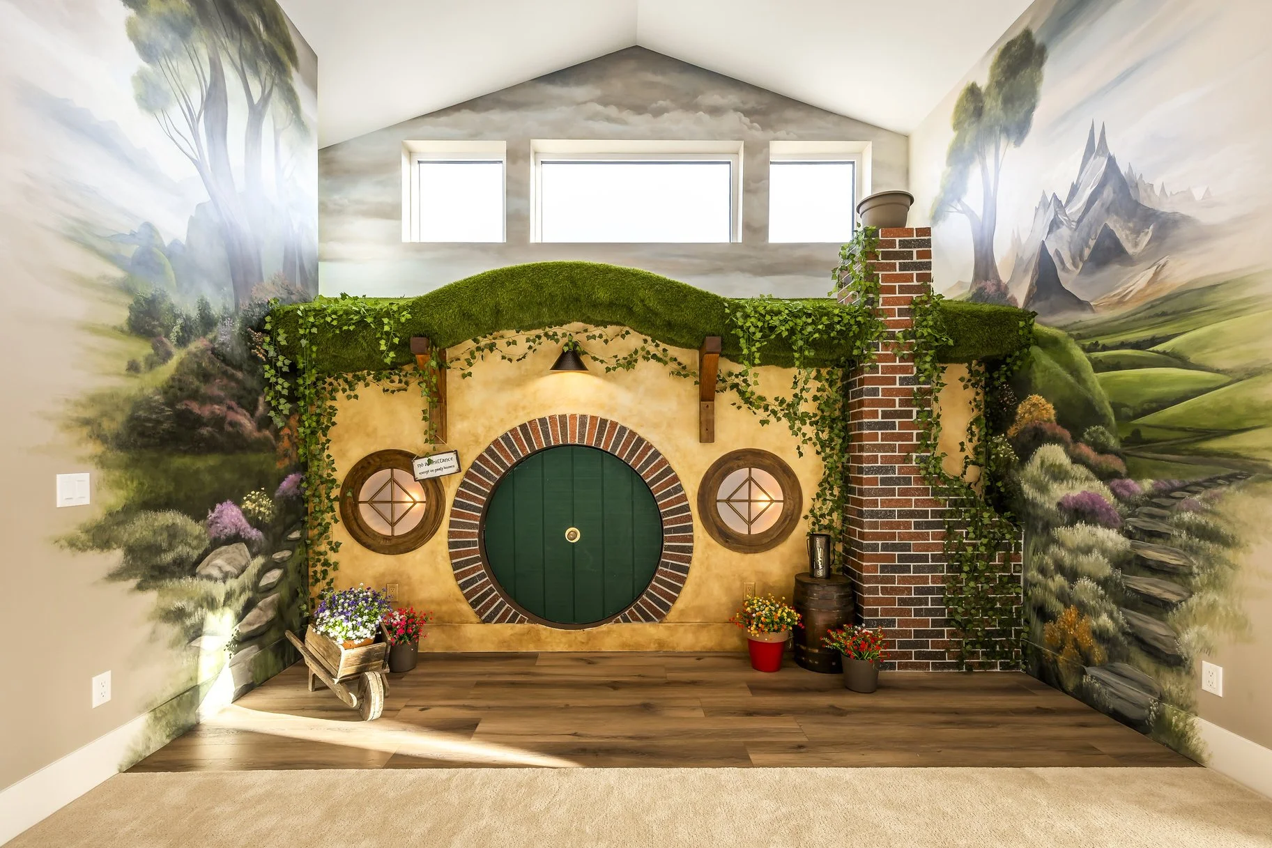Room decorated to resemble the Hobbit house from The Lord of the Rings with painted walls, a green door, circular windows, a faux chimney, and plants.