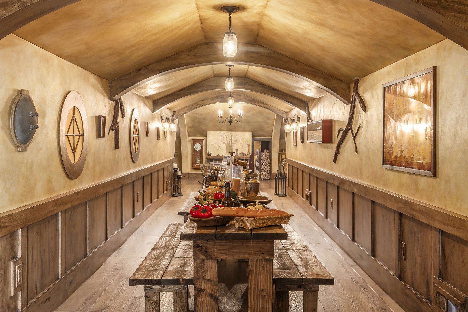 A rustic dining room with wooden furniture, a long table set with vegetables and beverages, and warm lighting fixtures on the ceiling and walls.