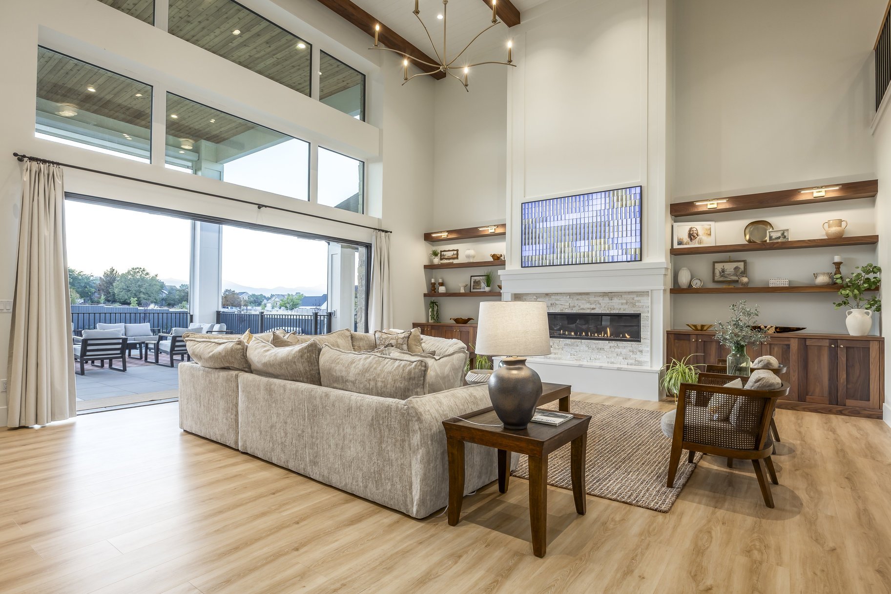 Spacious living room with large windows, a beige sofa, wooden shelves, and a modern fireplace.