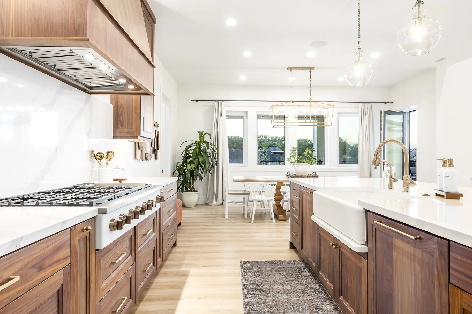Modern kitchen with wooden cabinets, white countertops, a large farmhouse sink, and a view of a dining area with large windows and a sliding door.