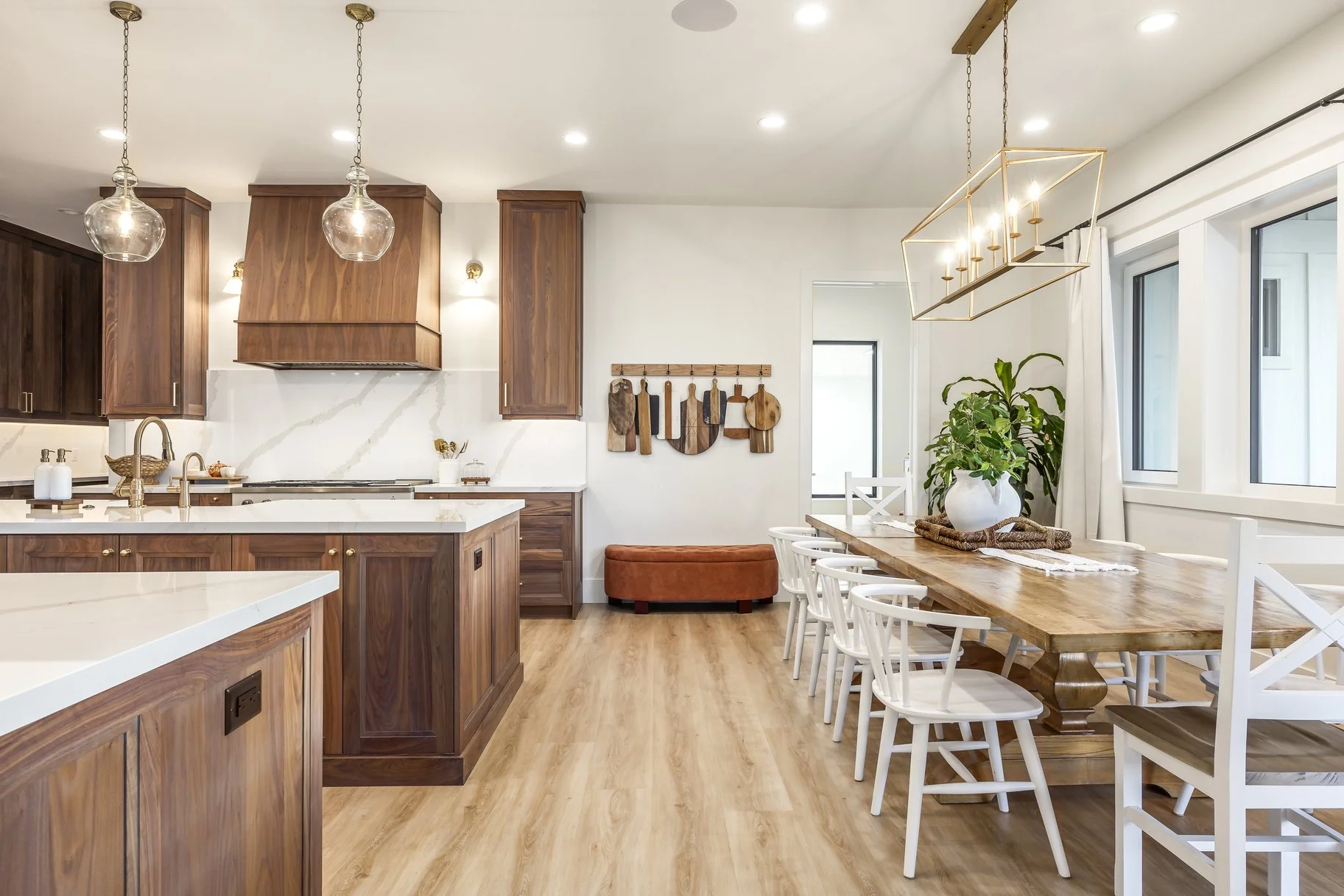 Bright kitchen and dining area with wooden cabinets, white countertops, a large dining table with white chairs, and pendant and chandelier lighting.