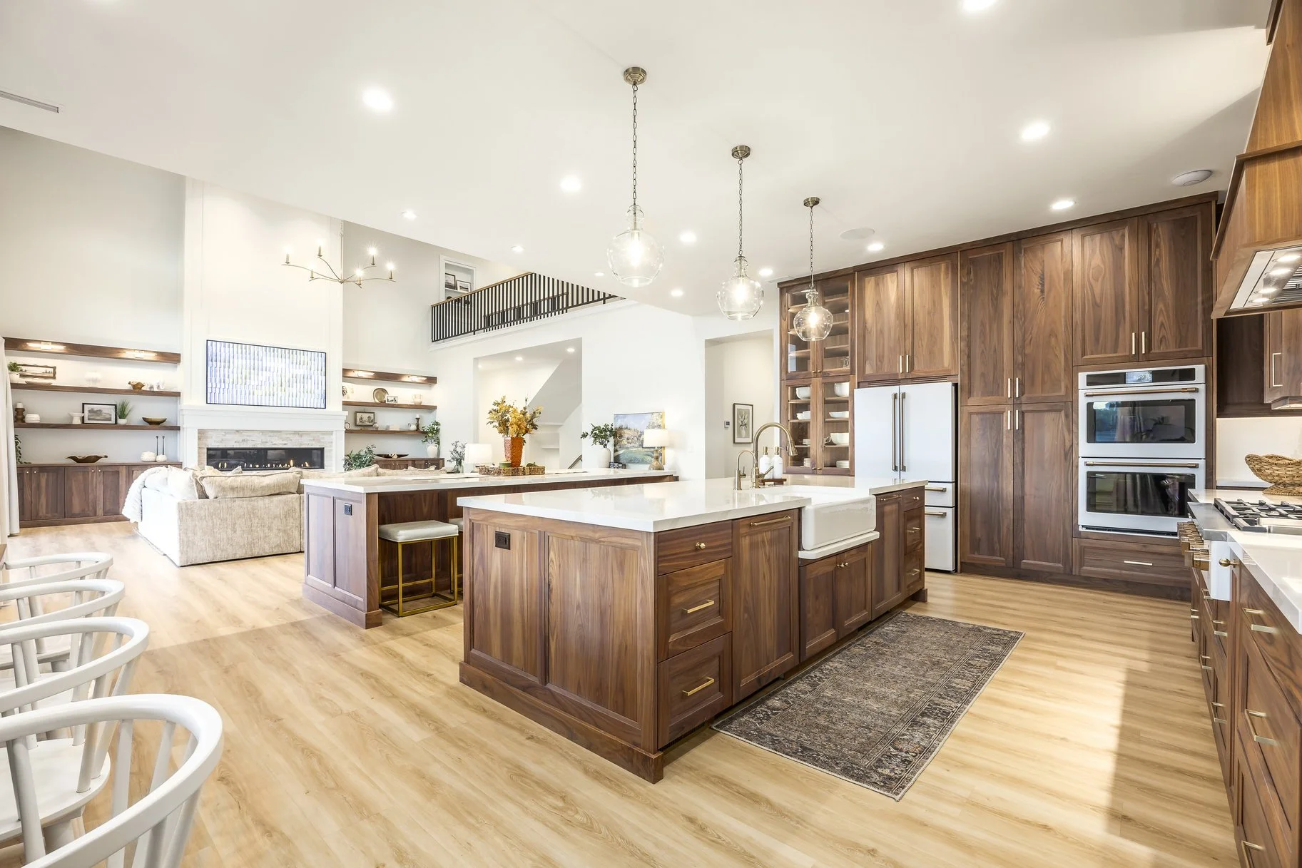 Modern open-concept kitchen and living room with wooden cabinets, white countertops, kitchen island with barstool, and a cozy seating area with a fireplace.