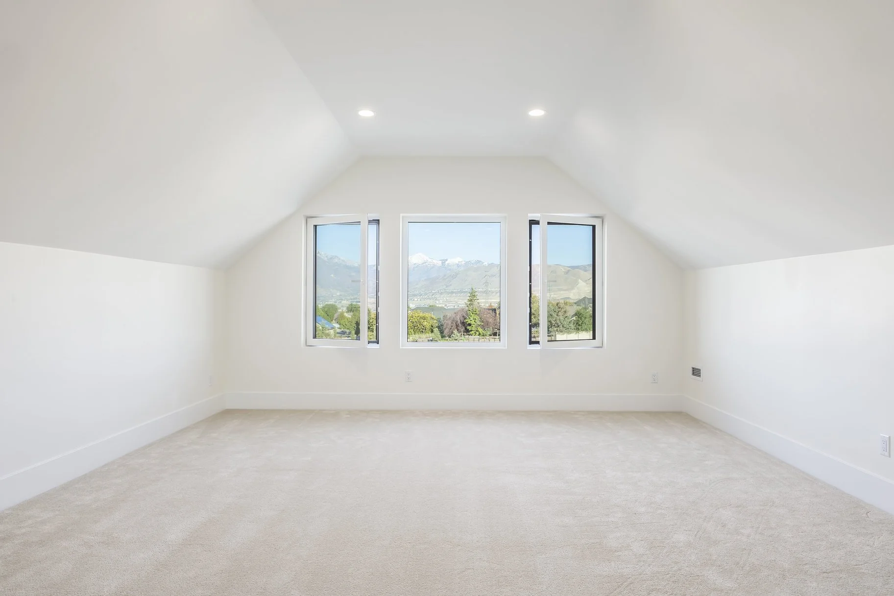 Empty white room with three large windows showing mountains and trees outside.
