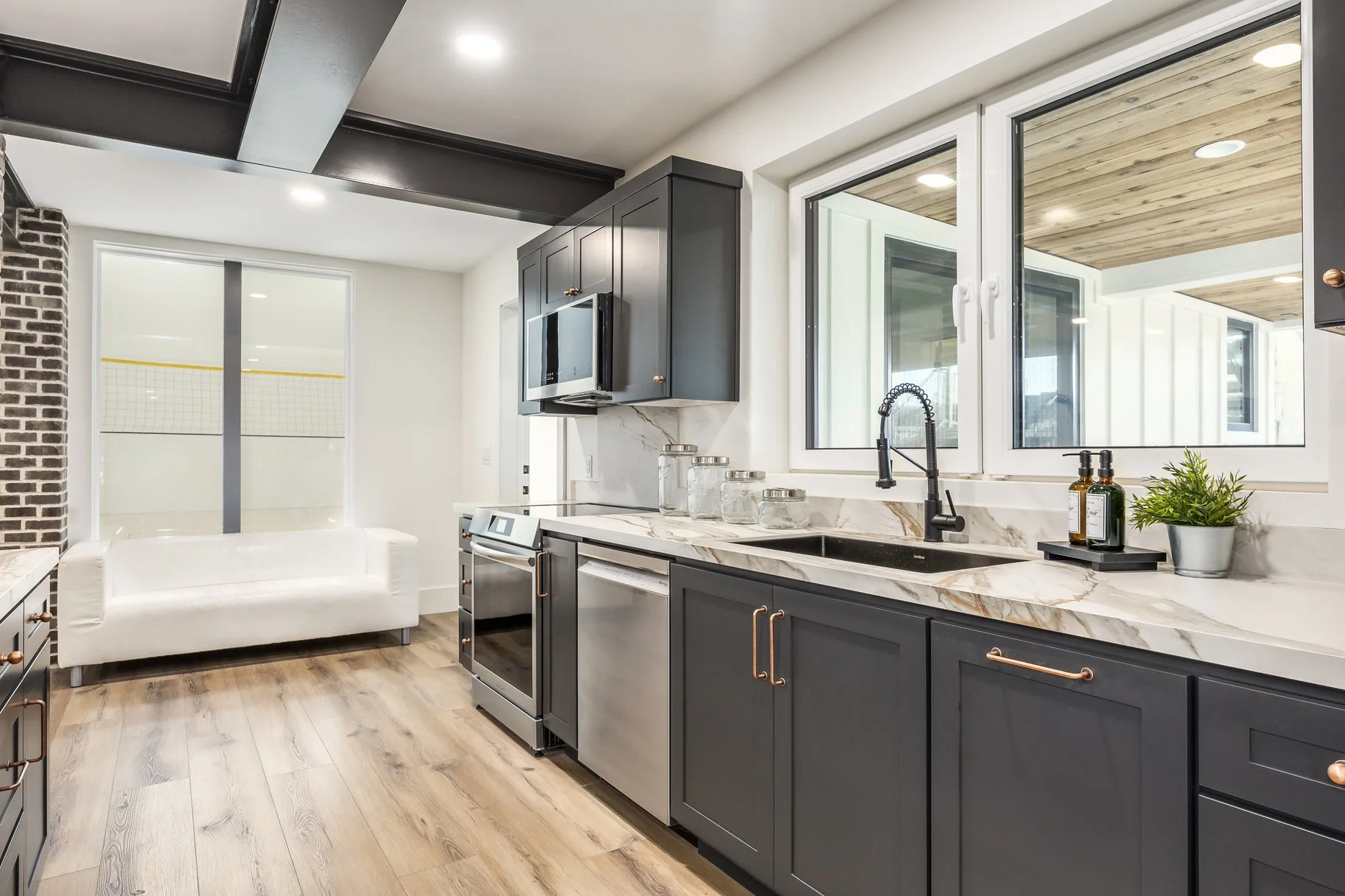 Modern kitchen with dark cabinets, stainless steel appliances, marble countertops, and large windows overlooking a porch with wooden ceiling.