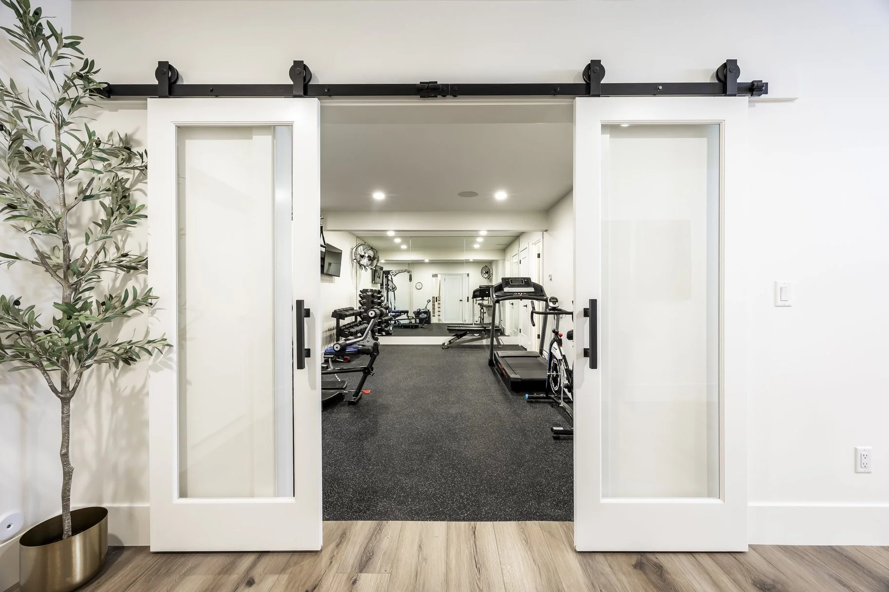 Fitness room with exercise equipment seen through glass sliding barn doors.