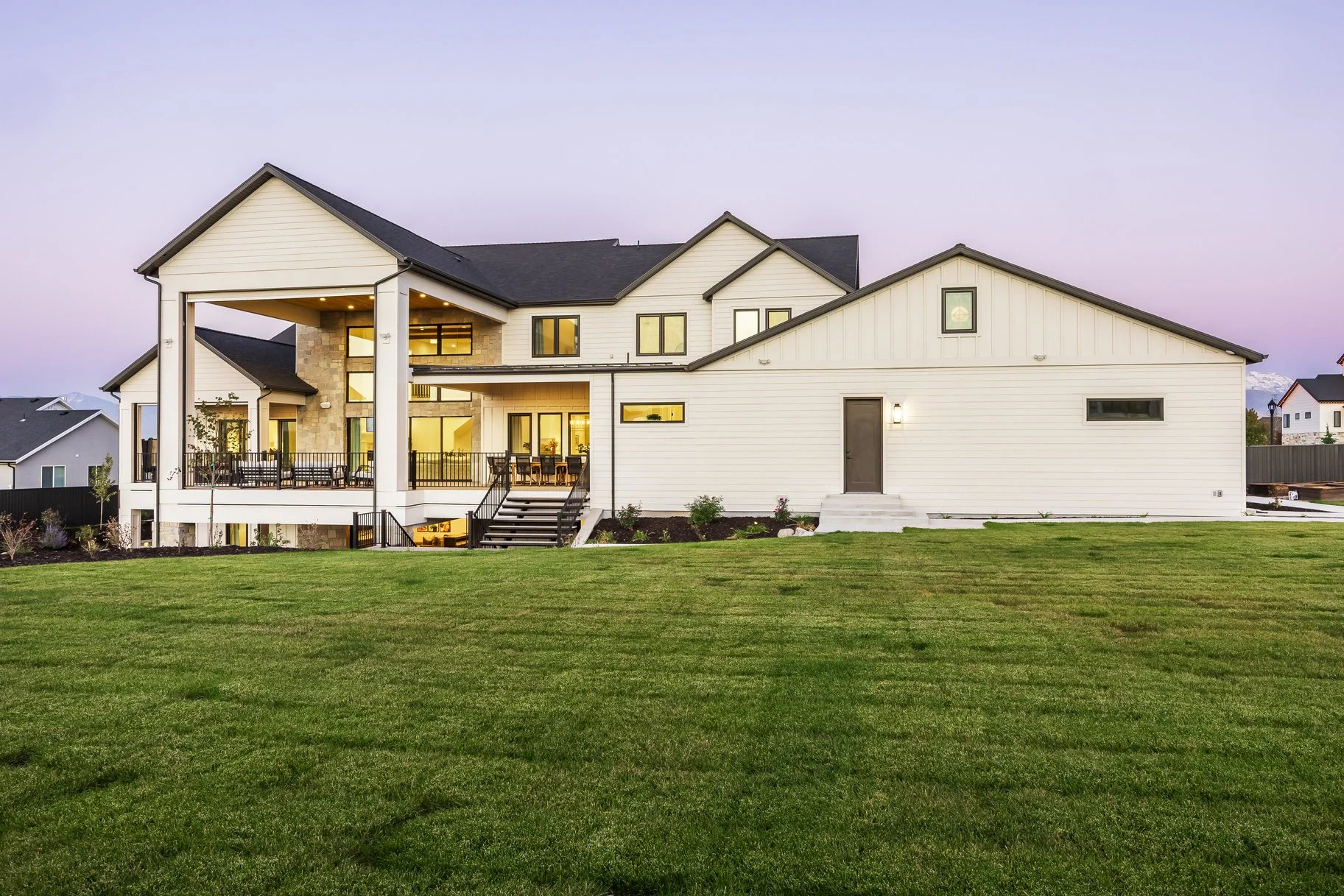 A modern two-story house with white siding, large windows, and a spacious backyard with green grass during twilight.