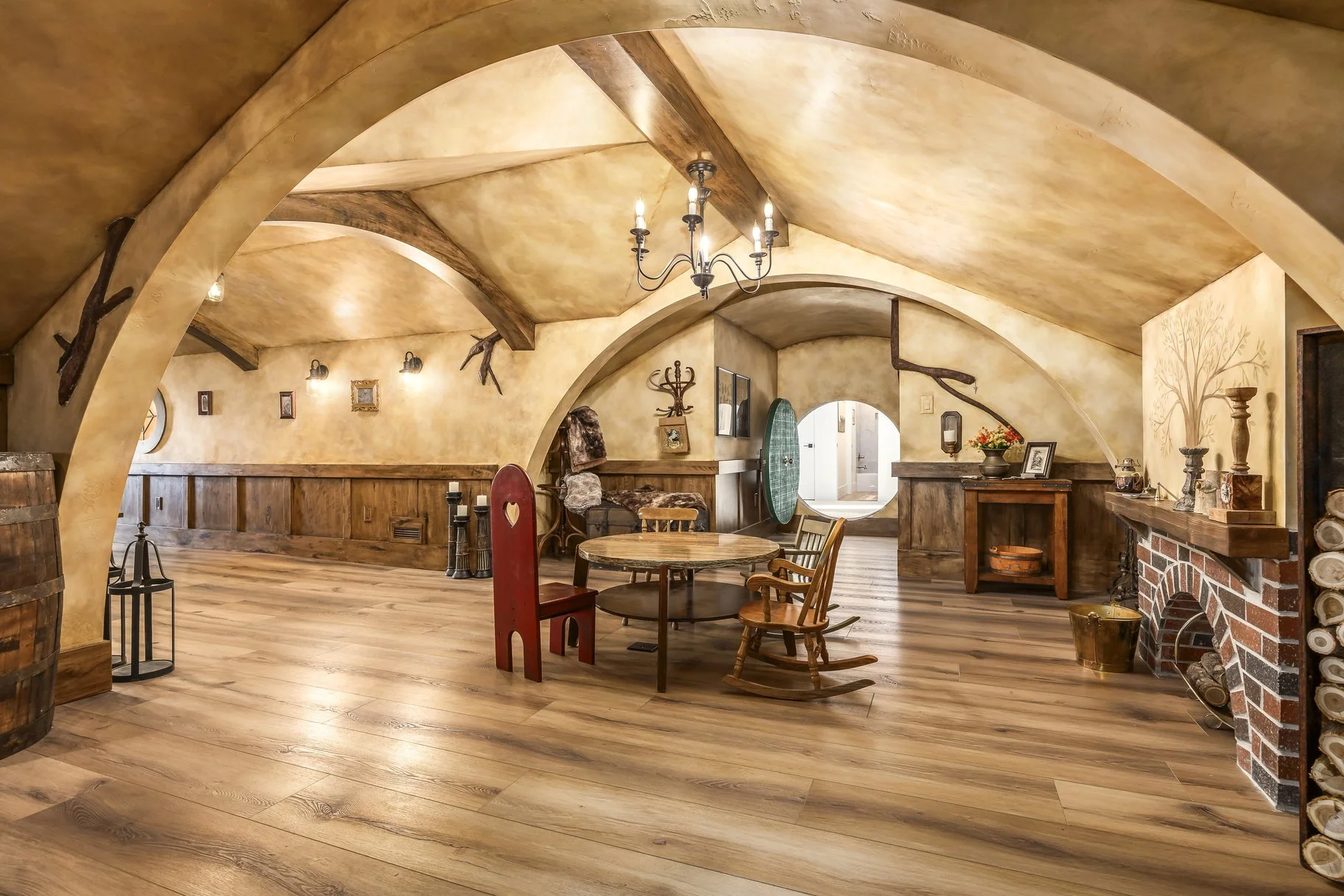 Rustic living room with arched ceilings and walls, wooden floor, vintage furniture, and decorative items including candlesticks, framed pictures, and a fireplace.