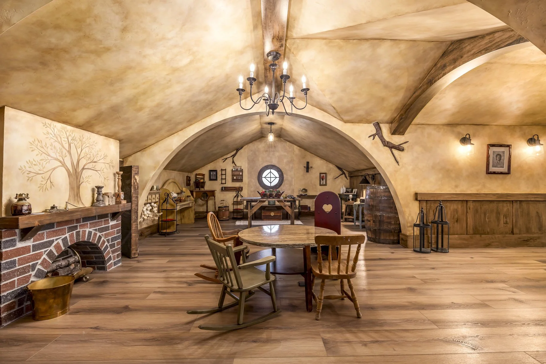 Cozy room with wooden floor, arched ceiling, chandelier, and vintage furniture, including a round table surrounded by four chairs, and decorative wall accents.