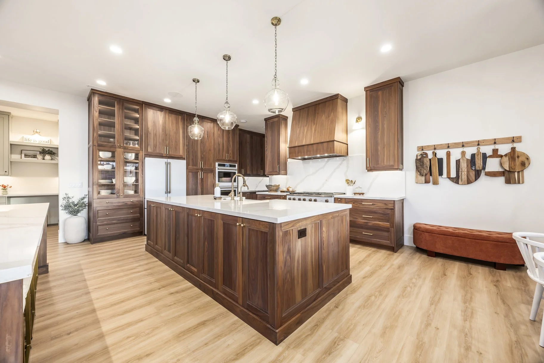 Modern kitchen with wooden cabinets, white marble island, and light wood flooring, featuring pendant lighting and wall-mounted cutting boards.