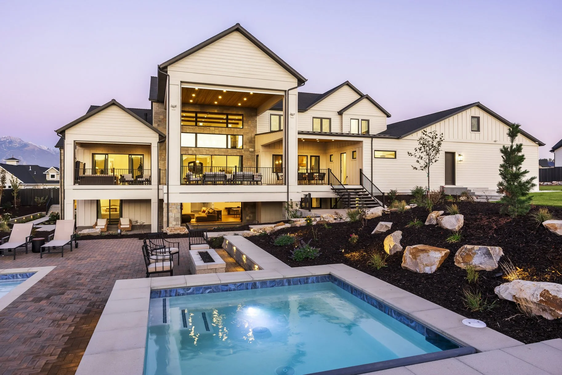 Modern house with multiple levels and large windows, outdoor swimming pool, landscaped yard, and outdoor seating area at sunset.