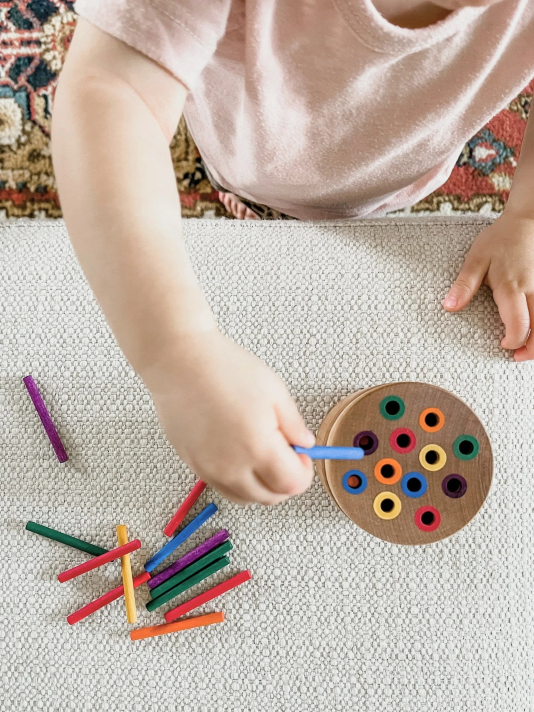 Child engaged in quiet tabletop activities while indoors. Playing with a colorful peg toy.