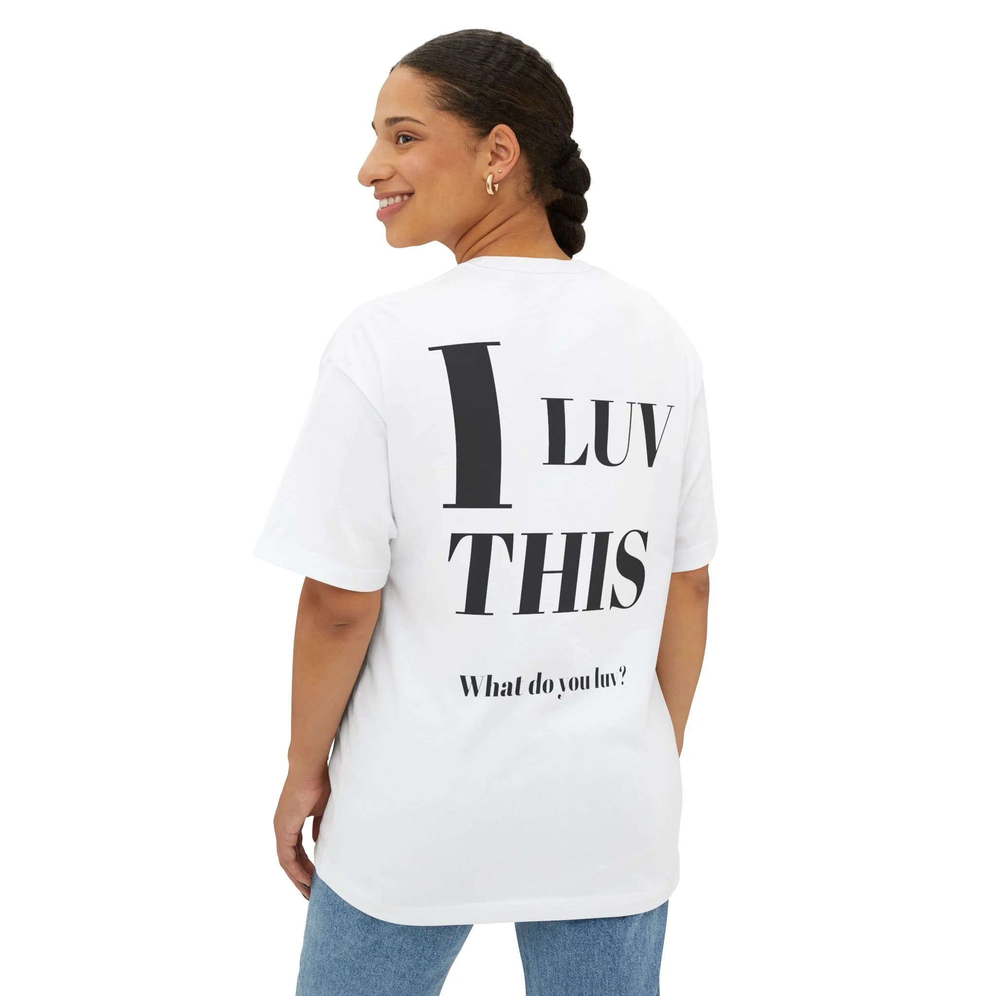 A woman wearing a white t-shirt with large black text that reads "I LUV THIS" and smaller text below that asks "What do you luv?". She has dark curly hair styled in a braid, earrings, and is smiling while looking to her left.