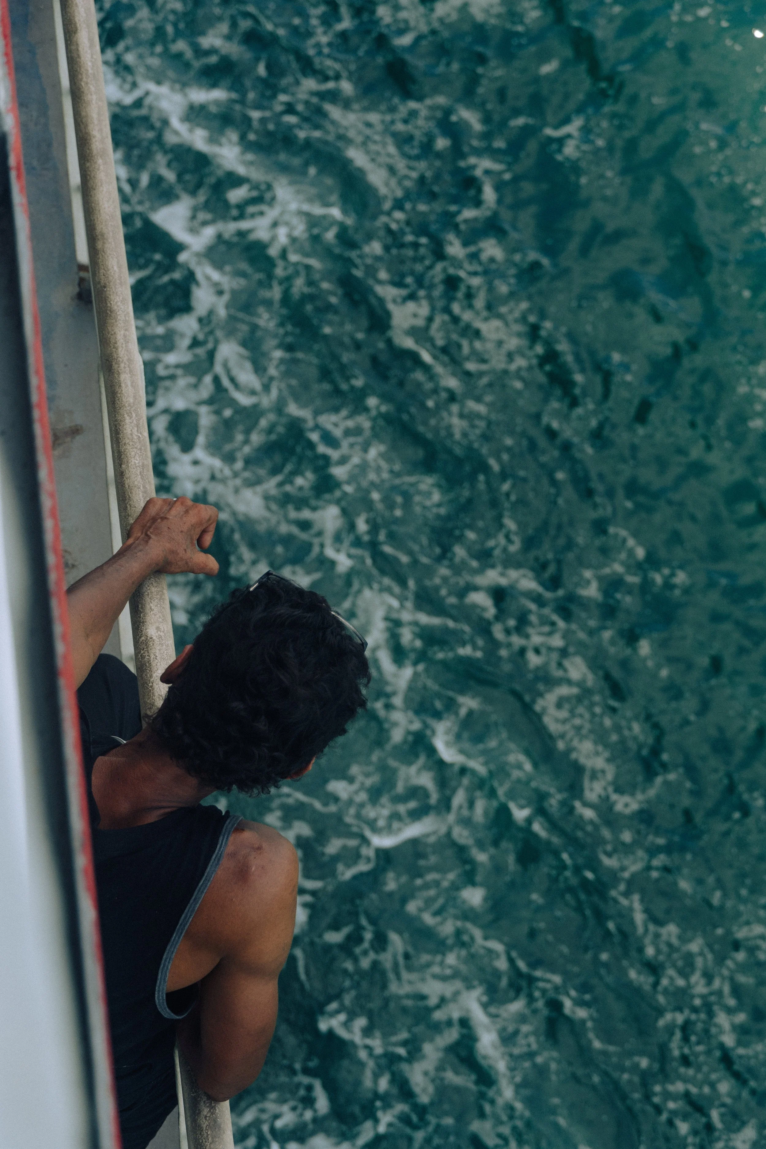 Two men leaning over the side of a boat, looking down at the water below.