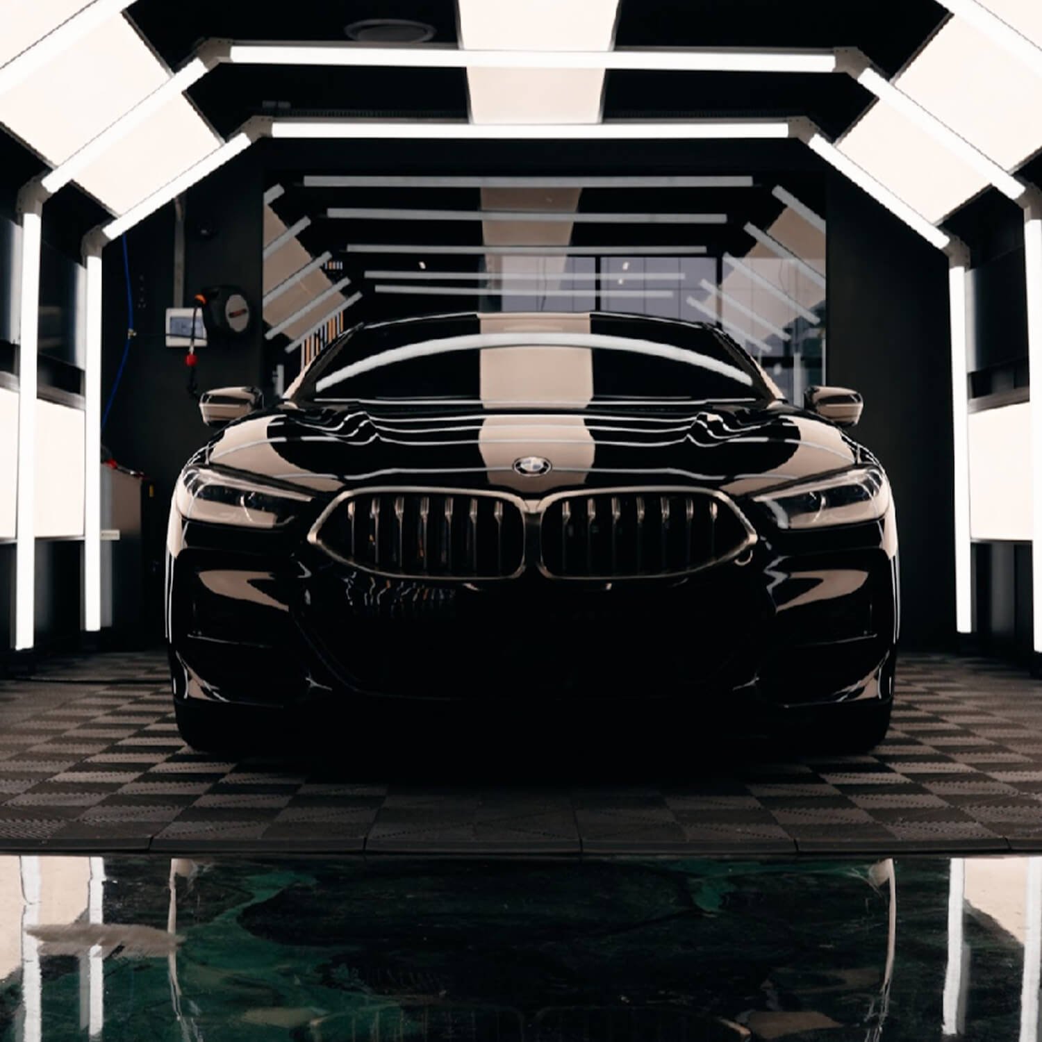 A black BMW car inside a modern, well-lit garage with reflective flooring.