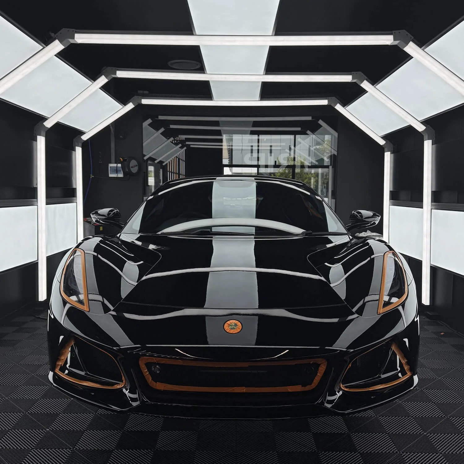 Black sports car inside a modern illuminated showroom with black walls and white lighting accents.