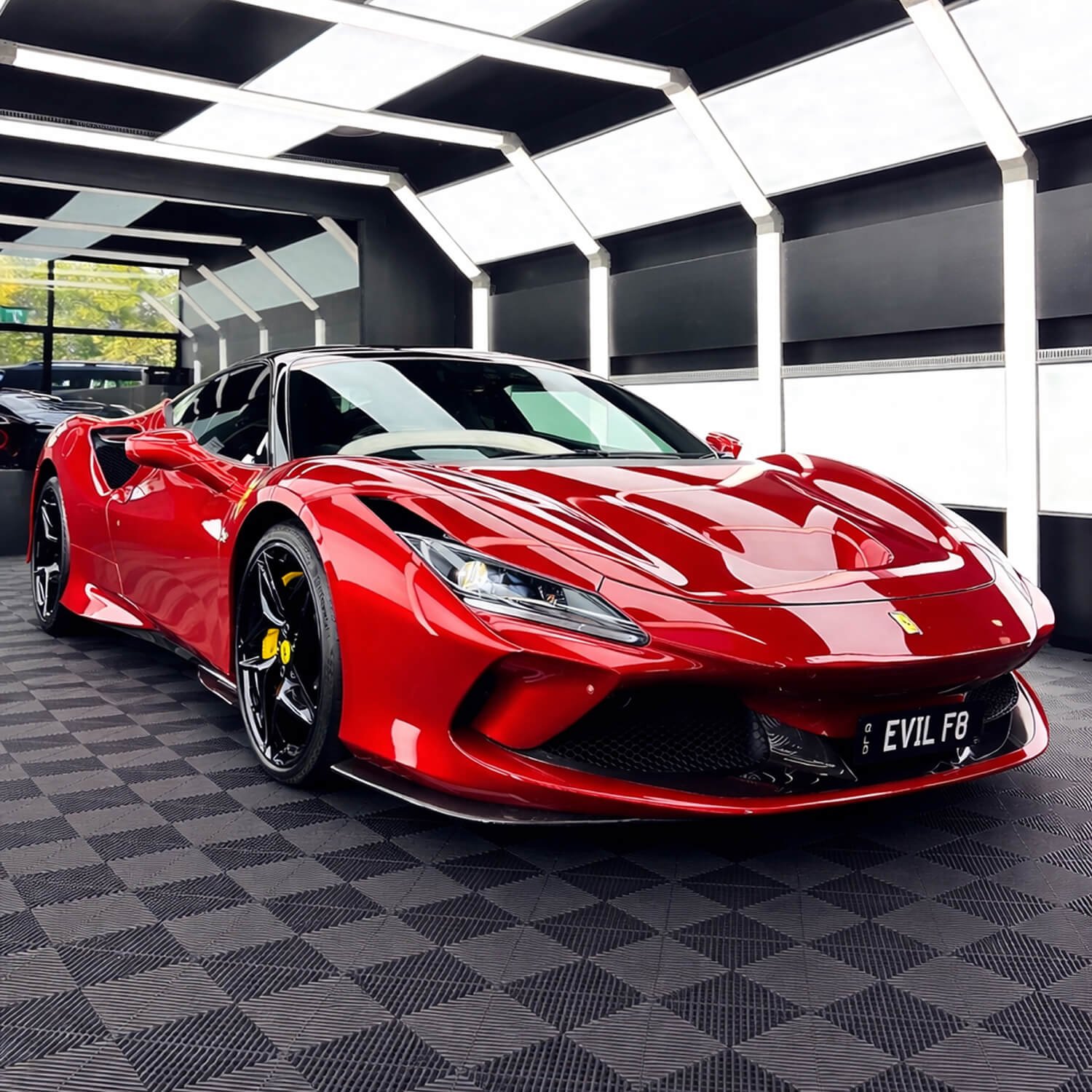 A red Ferrari sports car on display in a showroom with modern ceiling lighting and checkered flooring.