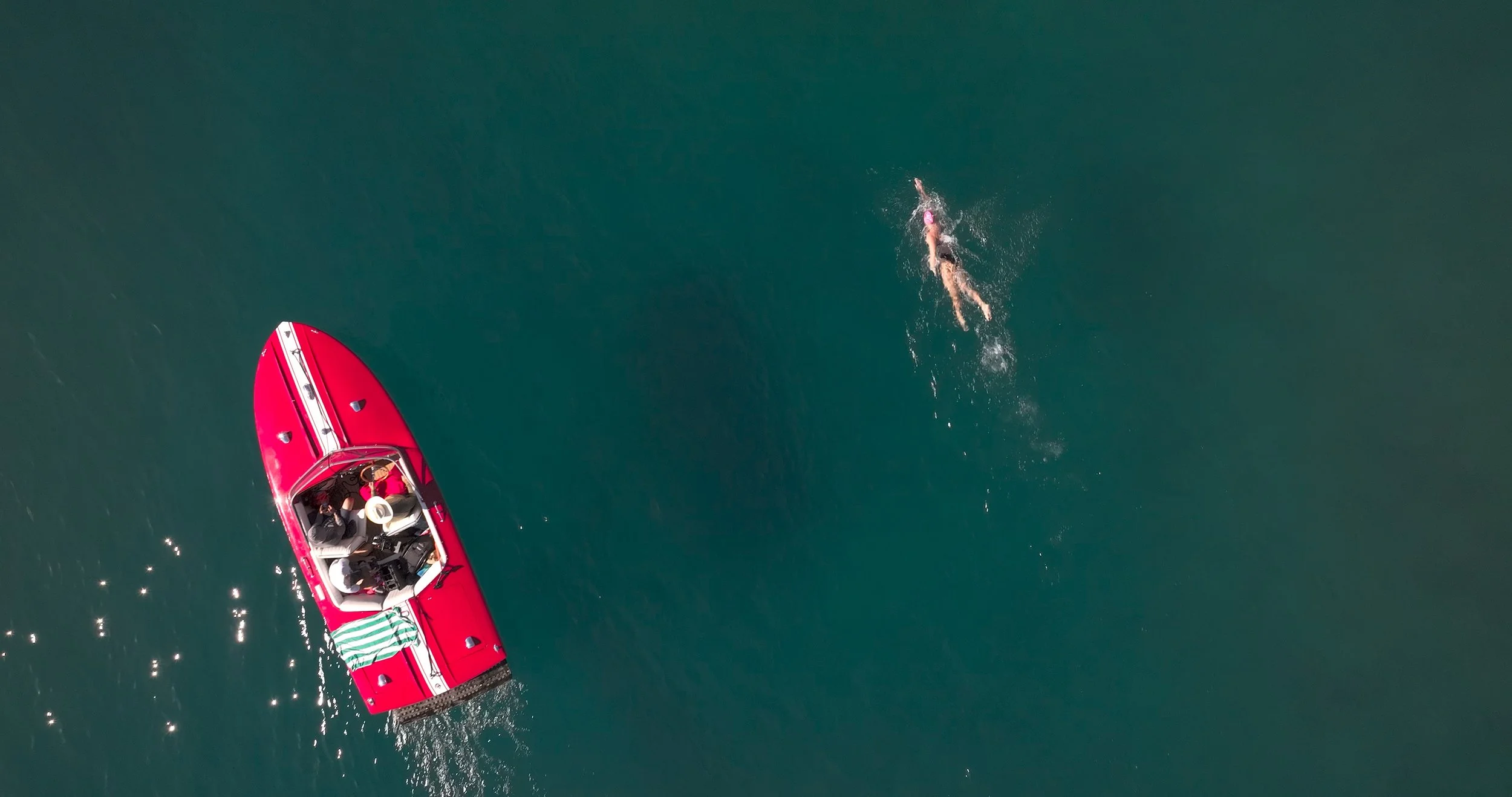 An aerial view of a person swimming in the water near a red speedboat.