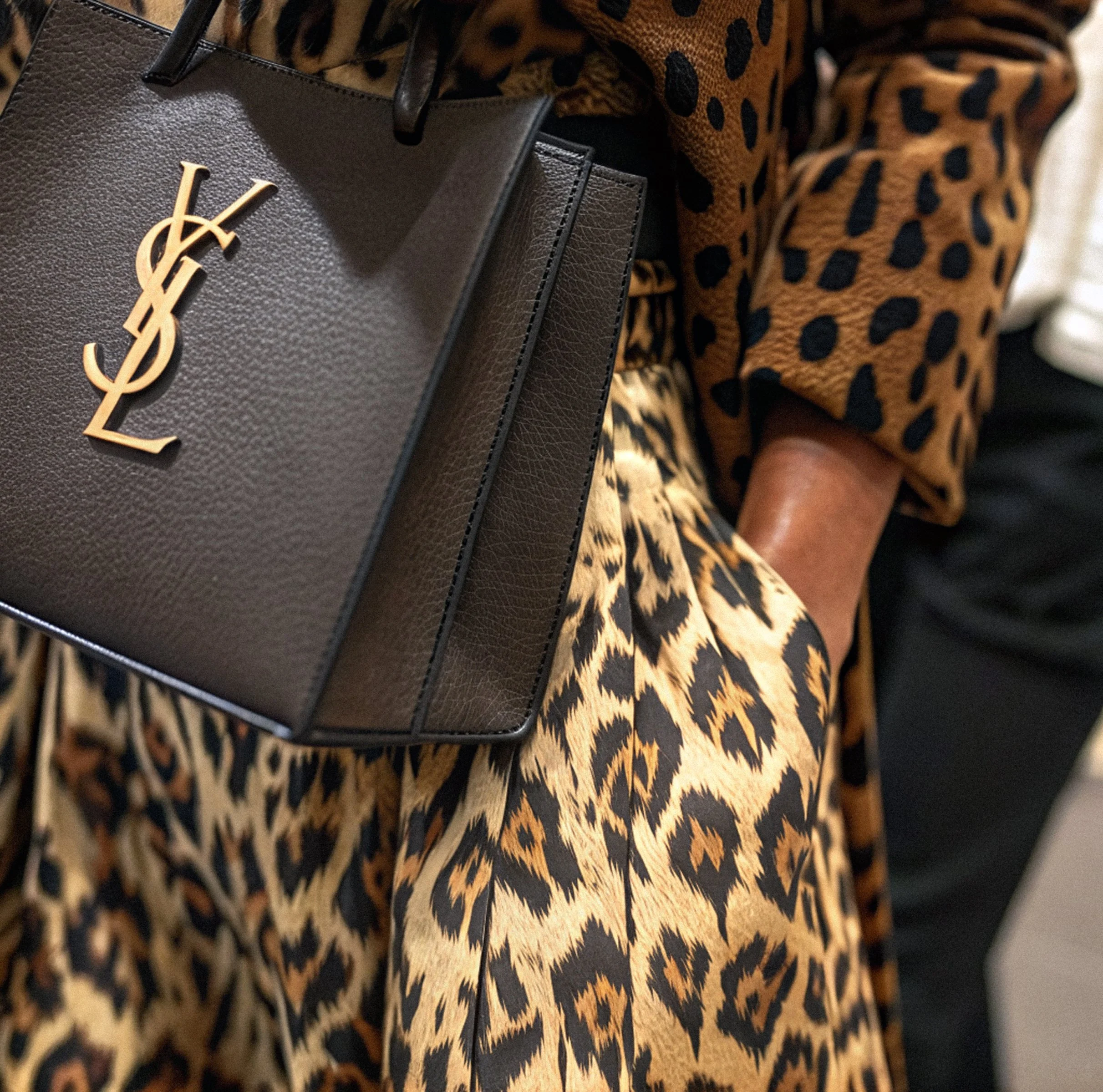 Close-up of a person holding a black Yves Saint Laurent handbag with a leopard print outfit.
