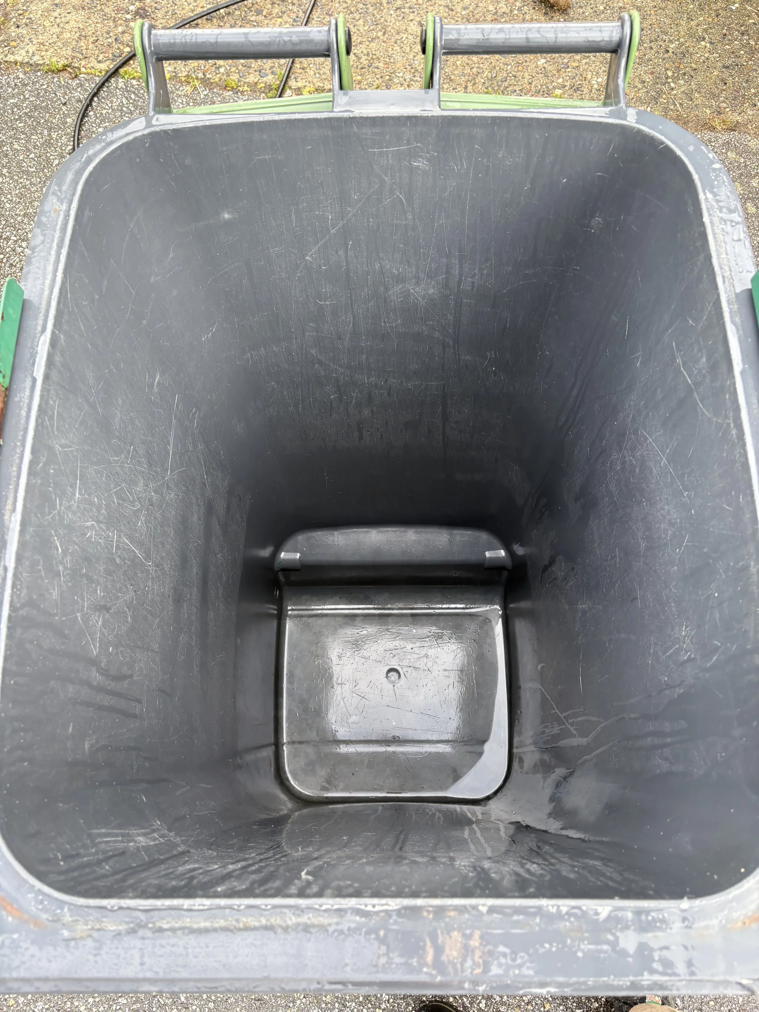 Empty black trash bin outdoors on a concrete surface.
