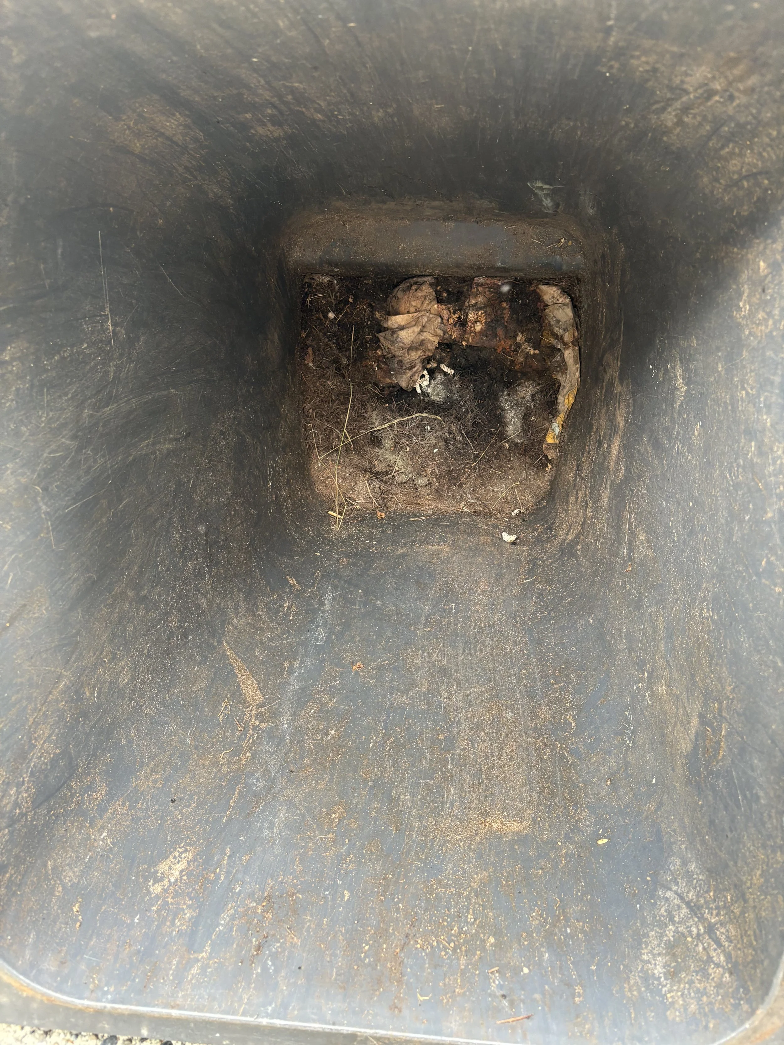 View looking inside a black cylindrical container with dirt, leaves, and debris at the bottom.