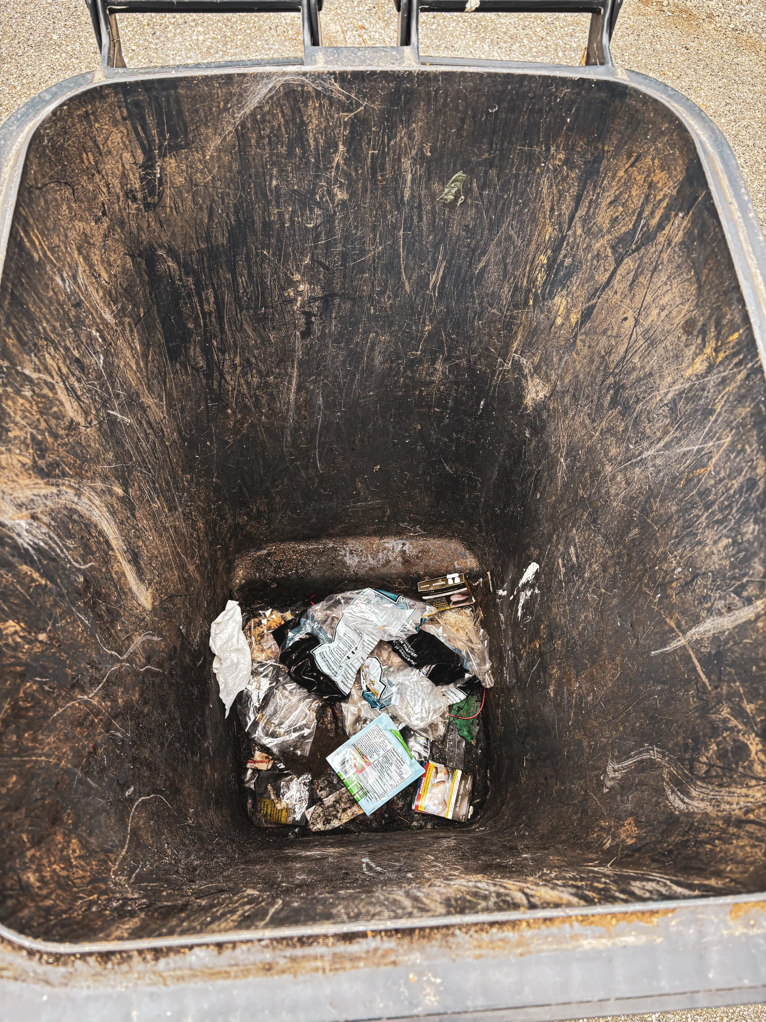 Inside a trash bin with crumpled plastic bags and miscellaneous waste at the bottom.