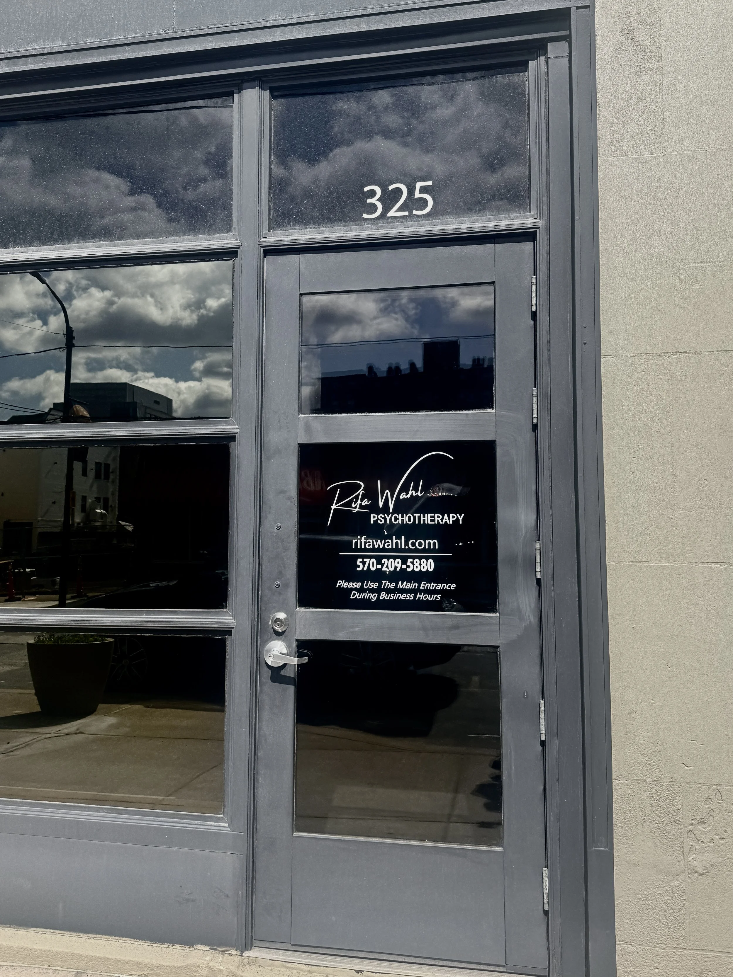 storefront door with the address 325 and a window sign for Rifa Wahl Psychotherapy with contact information.
