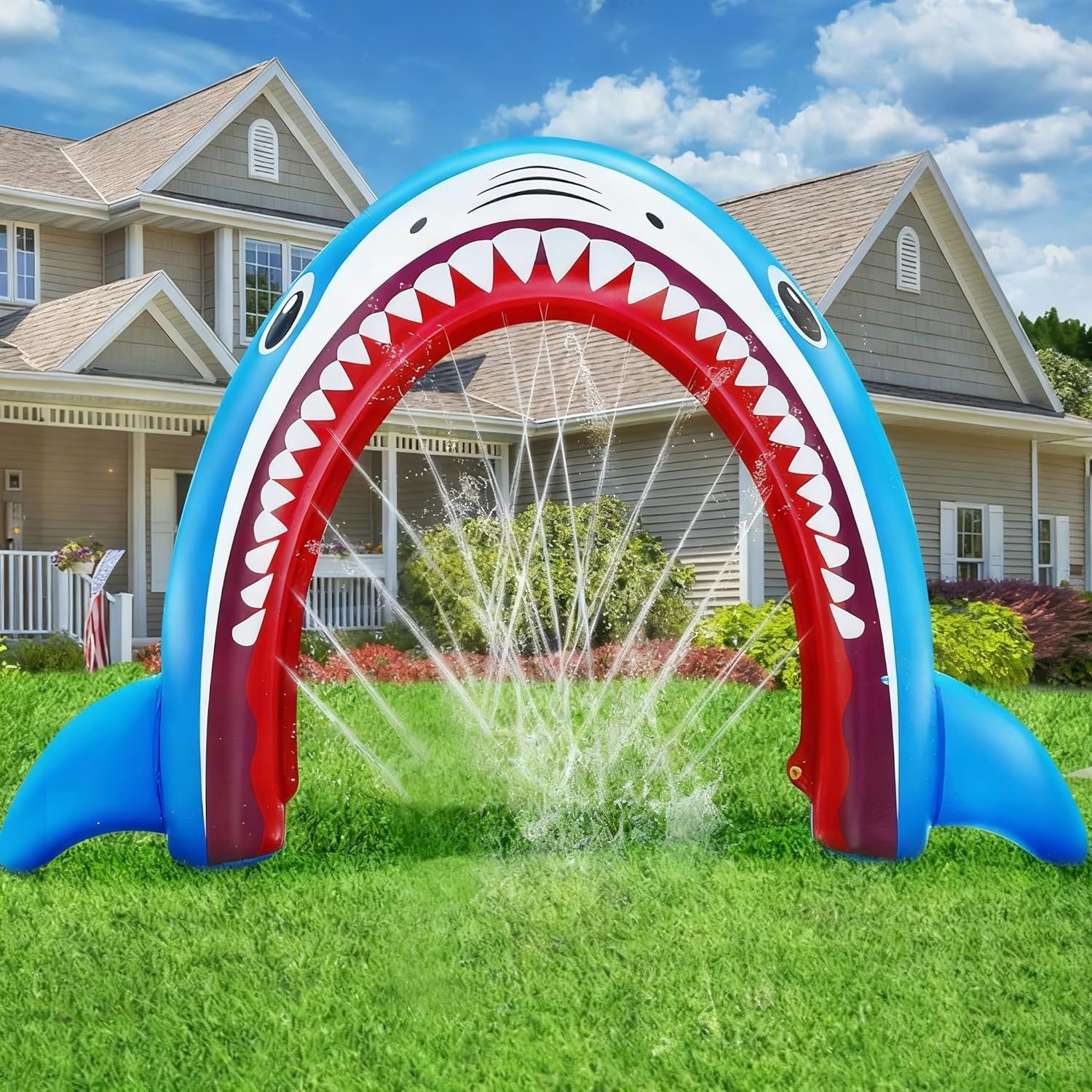 Inflatable shark-shaped water fountain with water spraying from its mouth, on a grassy lawn in front of a house with beige siding and a gabled roof.