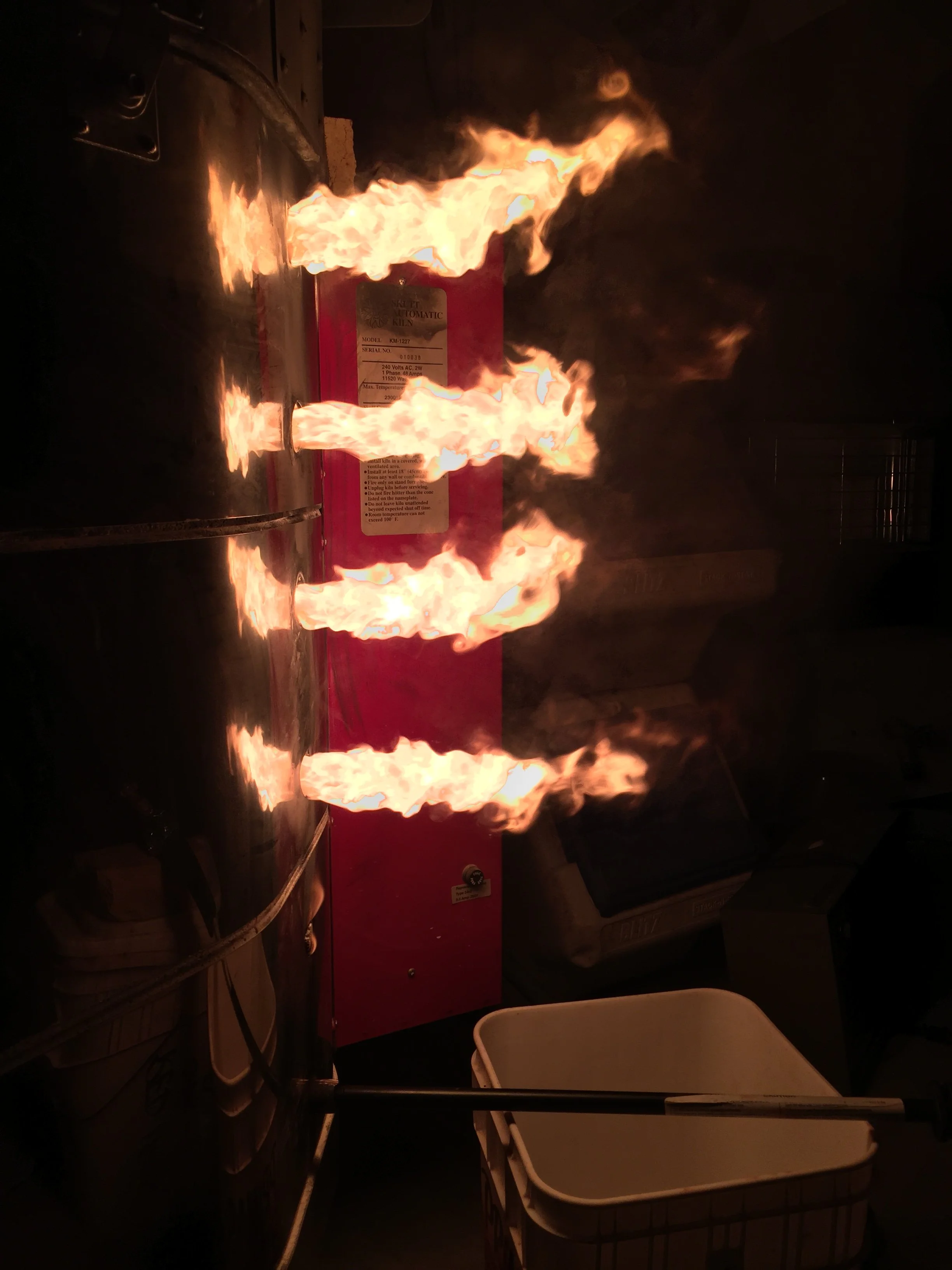 Flames roaring from a kiln burner port during a night firing