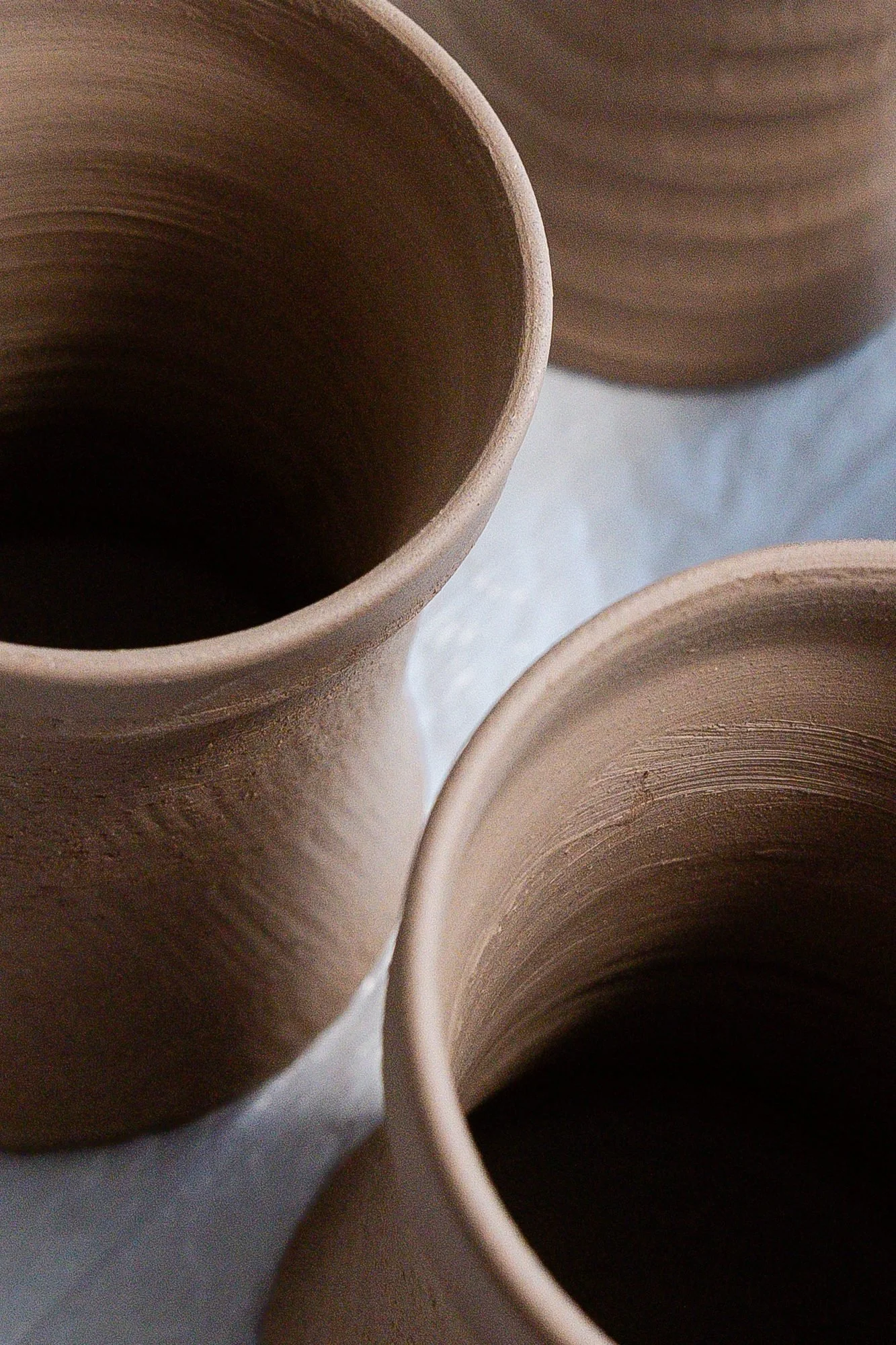 Close view of several unglazed thrown clay mug bodies with textured walls drying on a cloth covered table