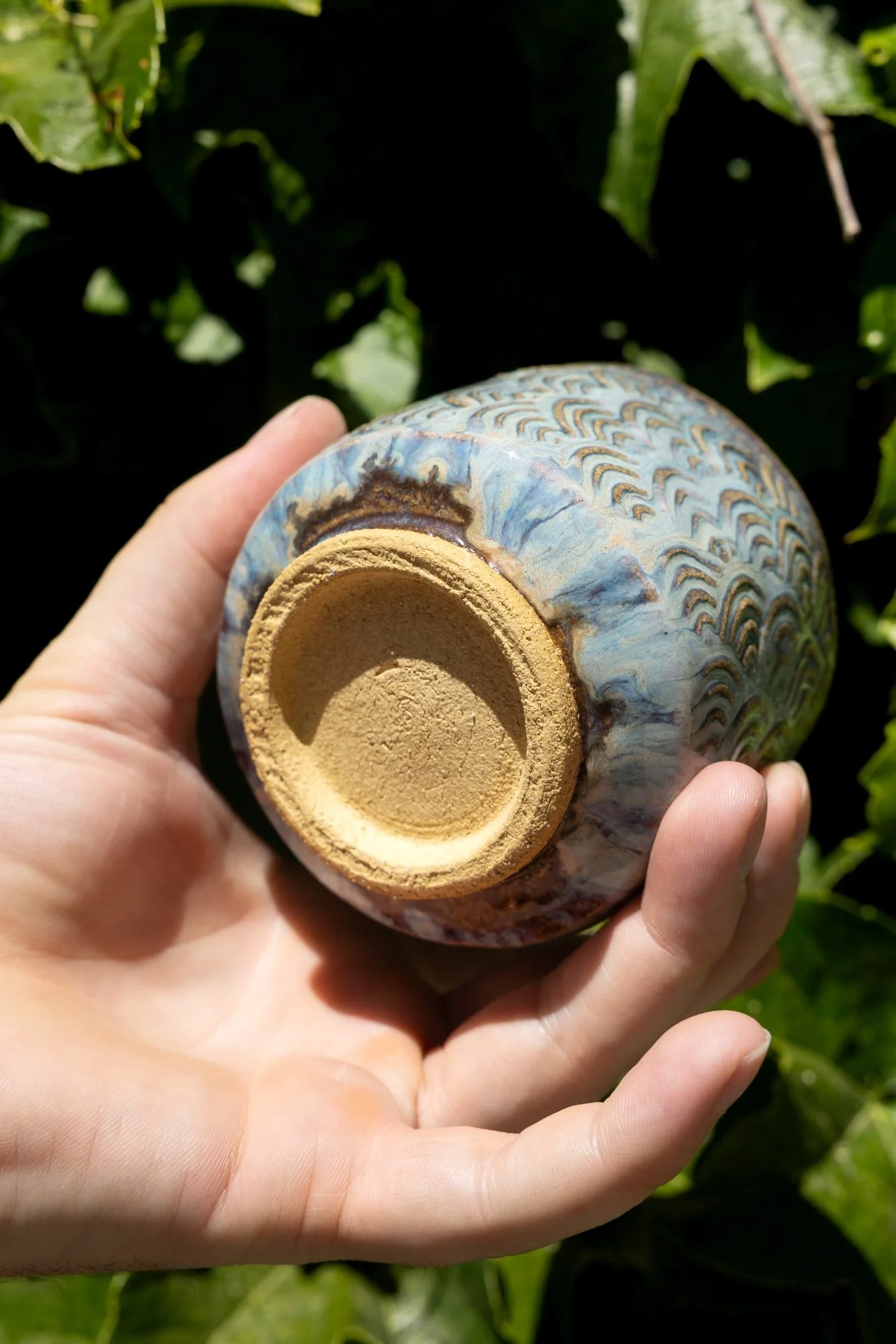 A hand holding a blue glazed cup upside down to show its bare unglazed clay foot ring