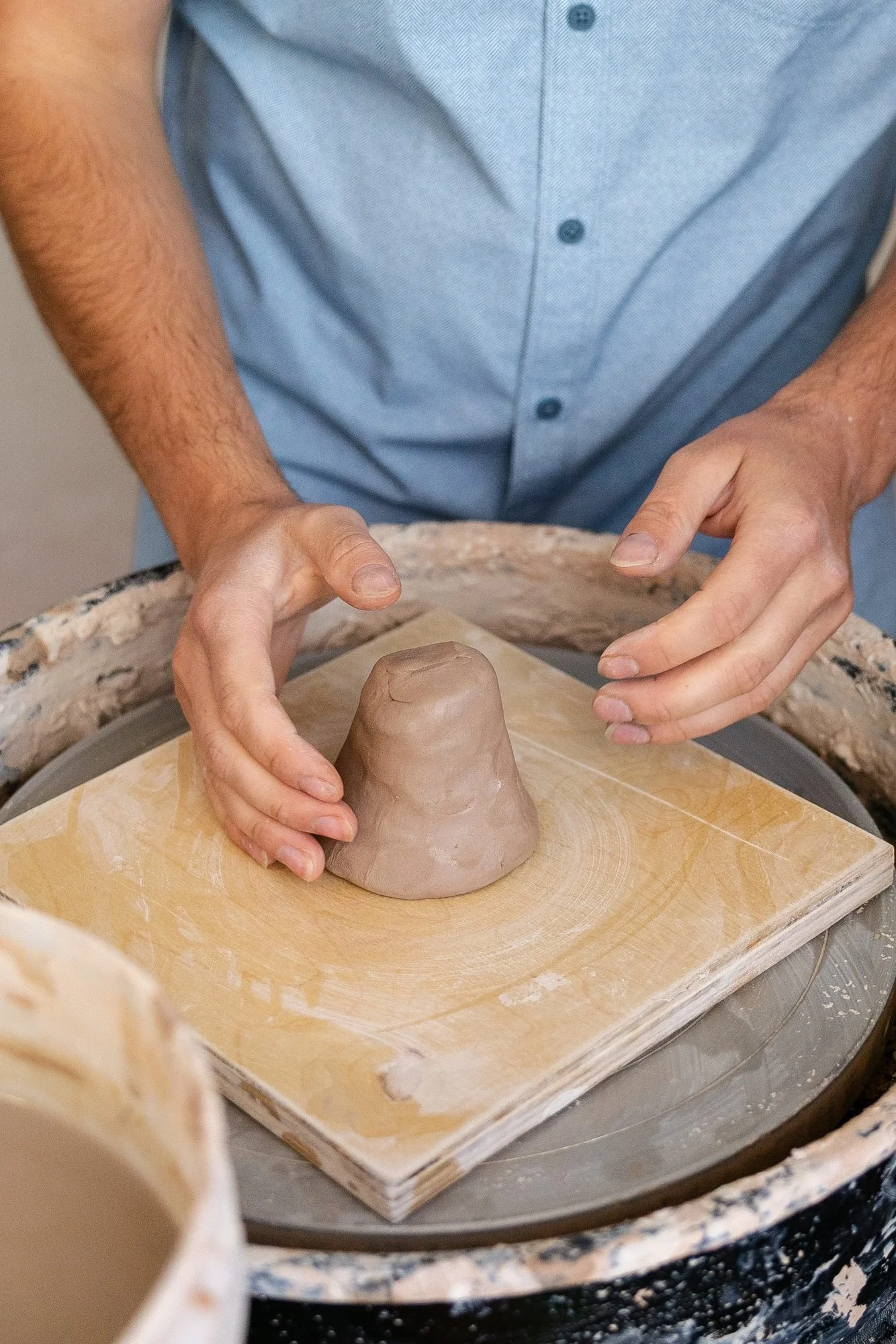 A single ball of clay sitting on a square plywood bat on a pottery wheel before centering