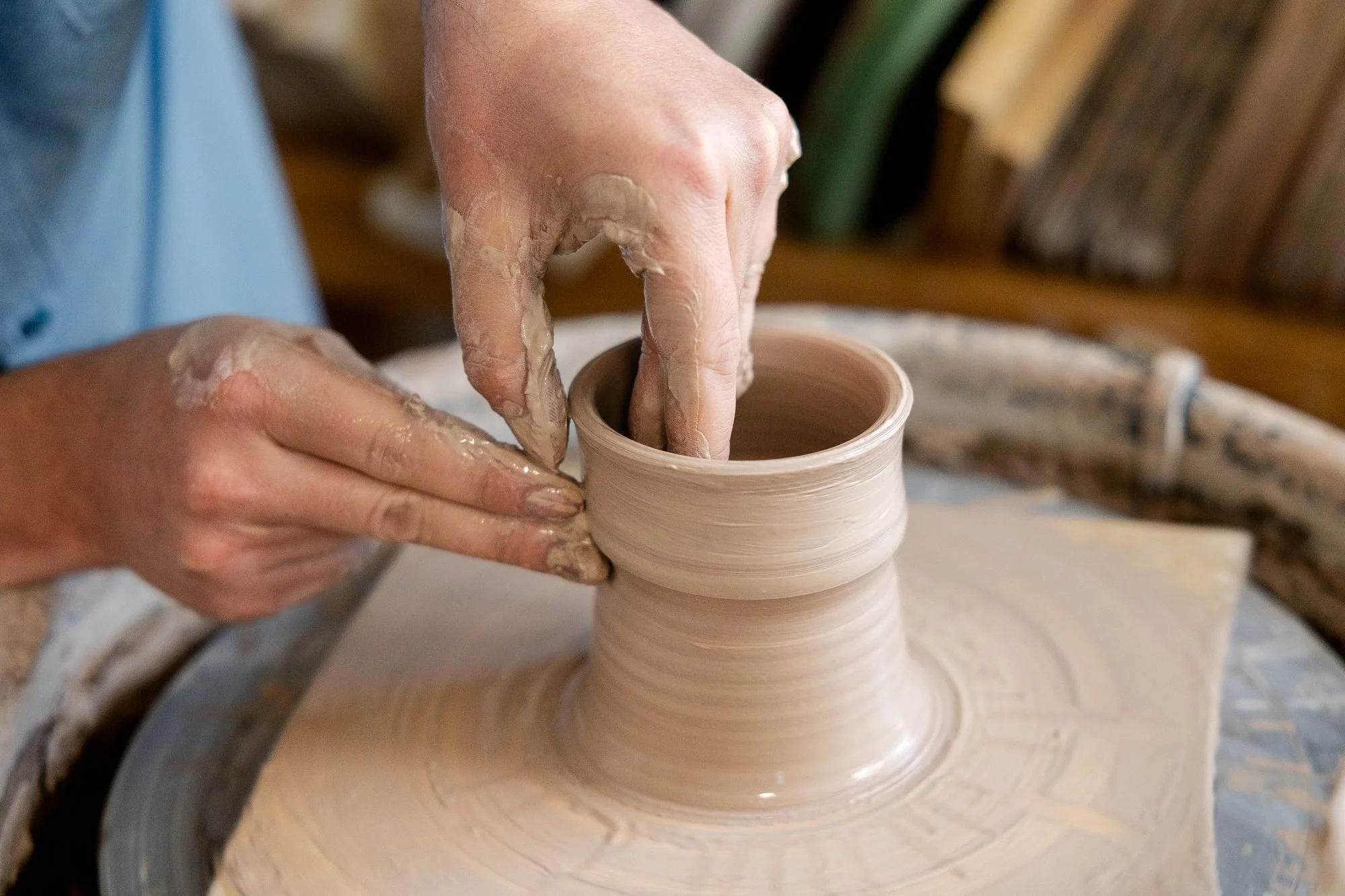 Two hands opening a short clay cylinder on the wheel, thumbs pressed inside and fingers supporting the outside wall