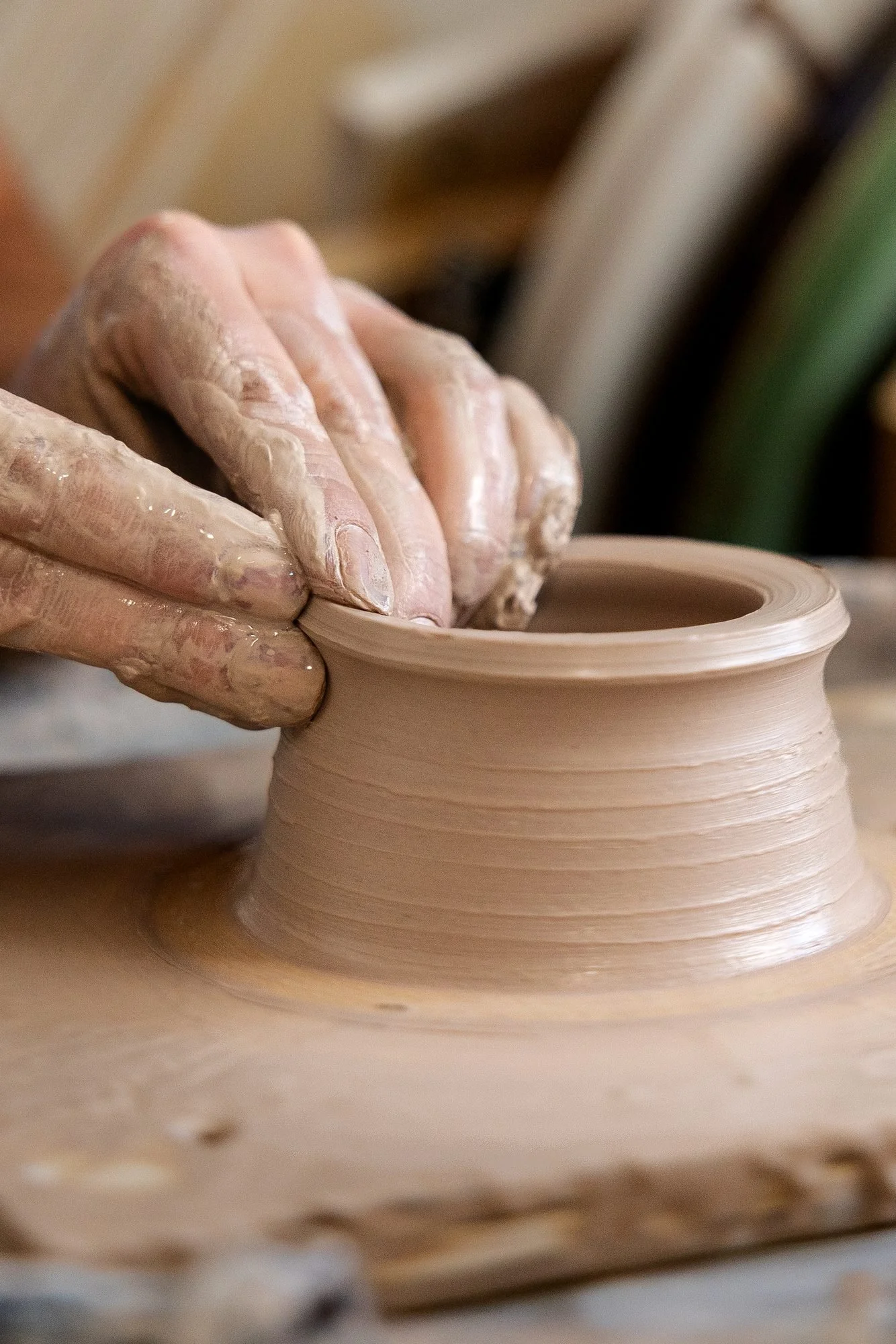 Fingertips on the inside and outside of a thin wet clay cylinder wall as it is pulled upward on the wheel