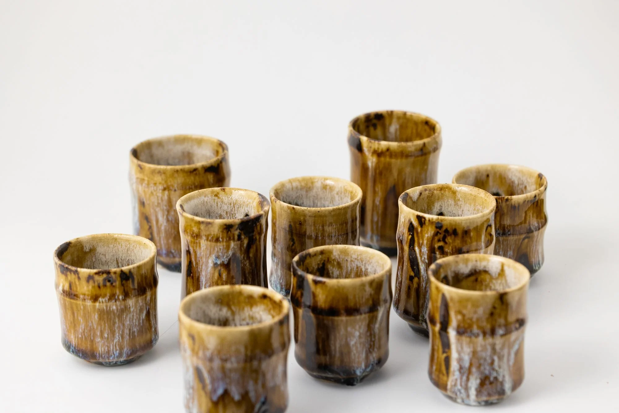 A group of salt glazed cups and tumblers in amber and brown tones arranged together on a white surface