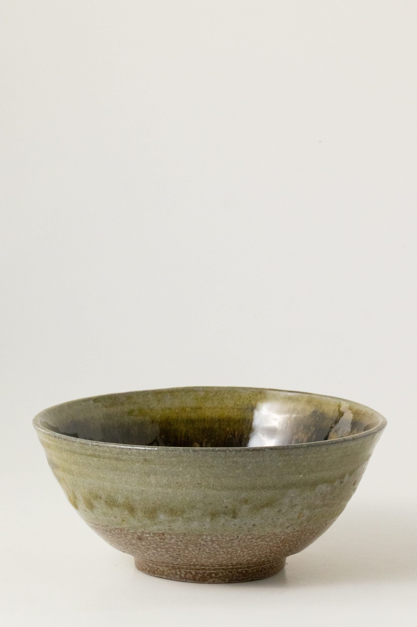 A wide shallow salt glazed bowl in olive green and brown tones on a white background