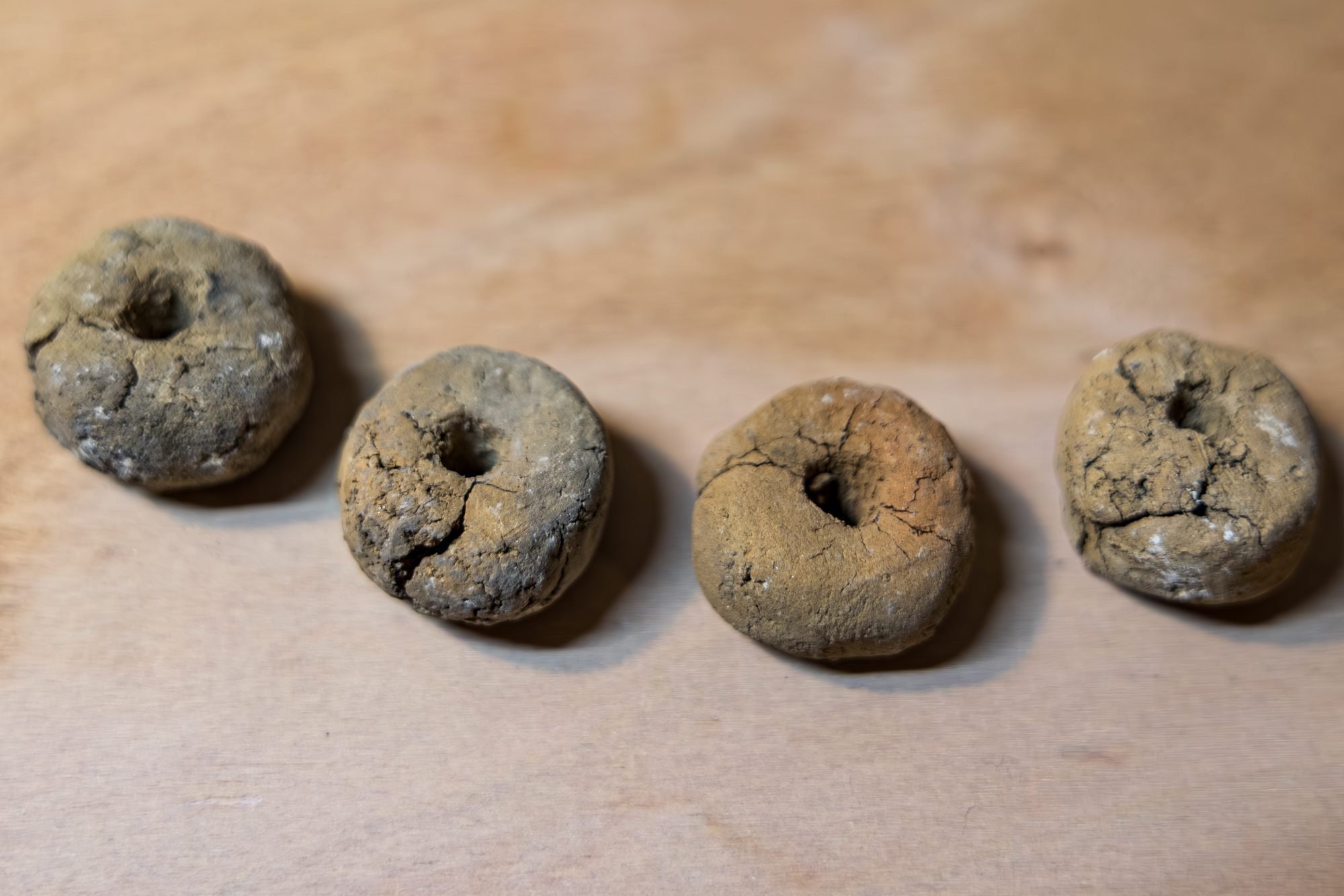 Four small rings of grey wild clay on a wooden table, two of them split by visible cracks
