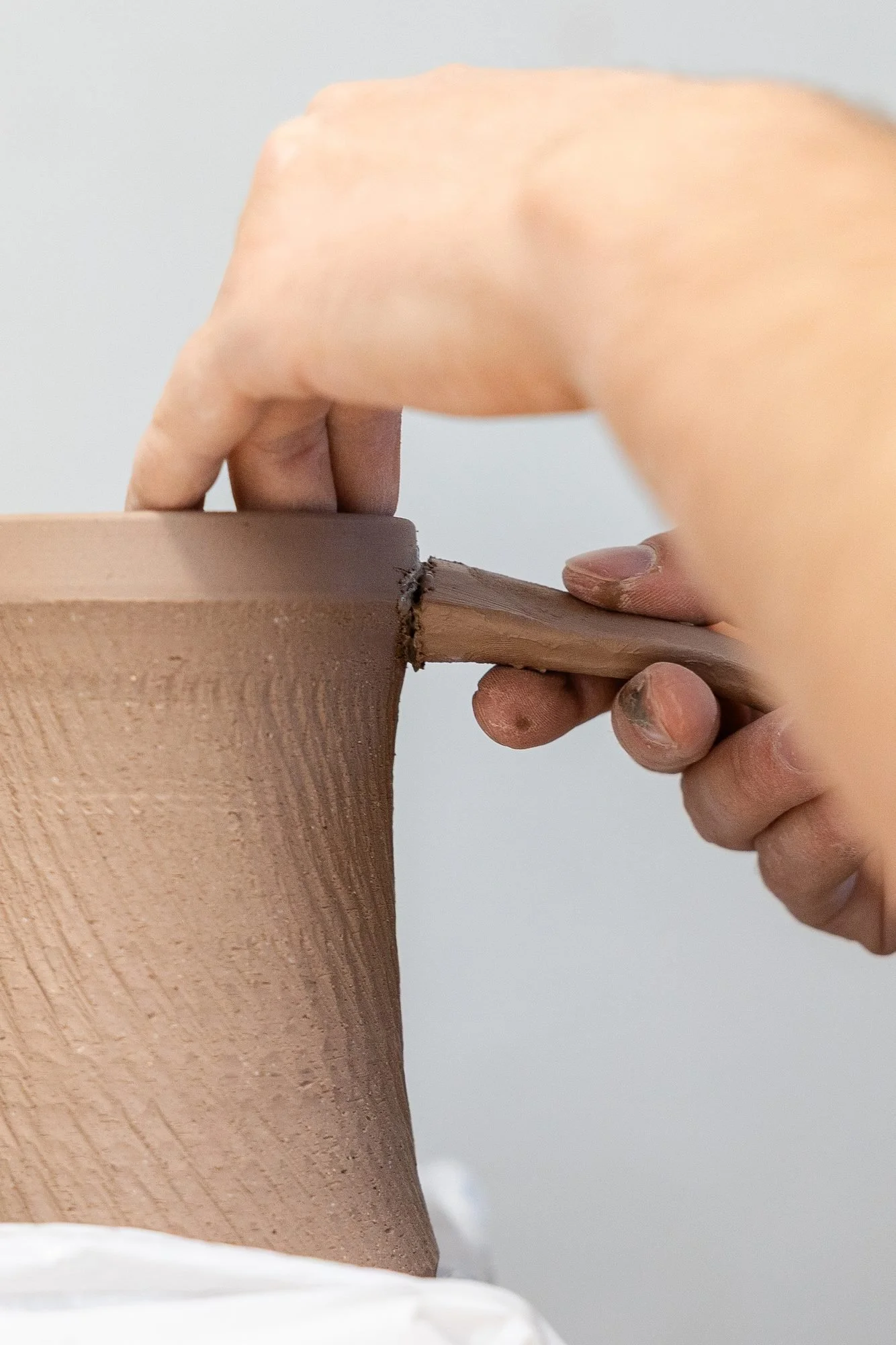 Two hands pressing the top of a pulled clay handle against the rim area of a textured mug