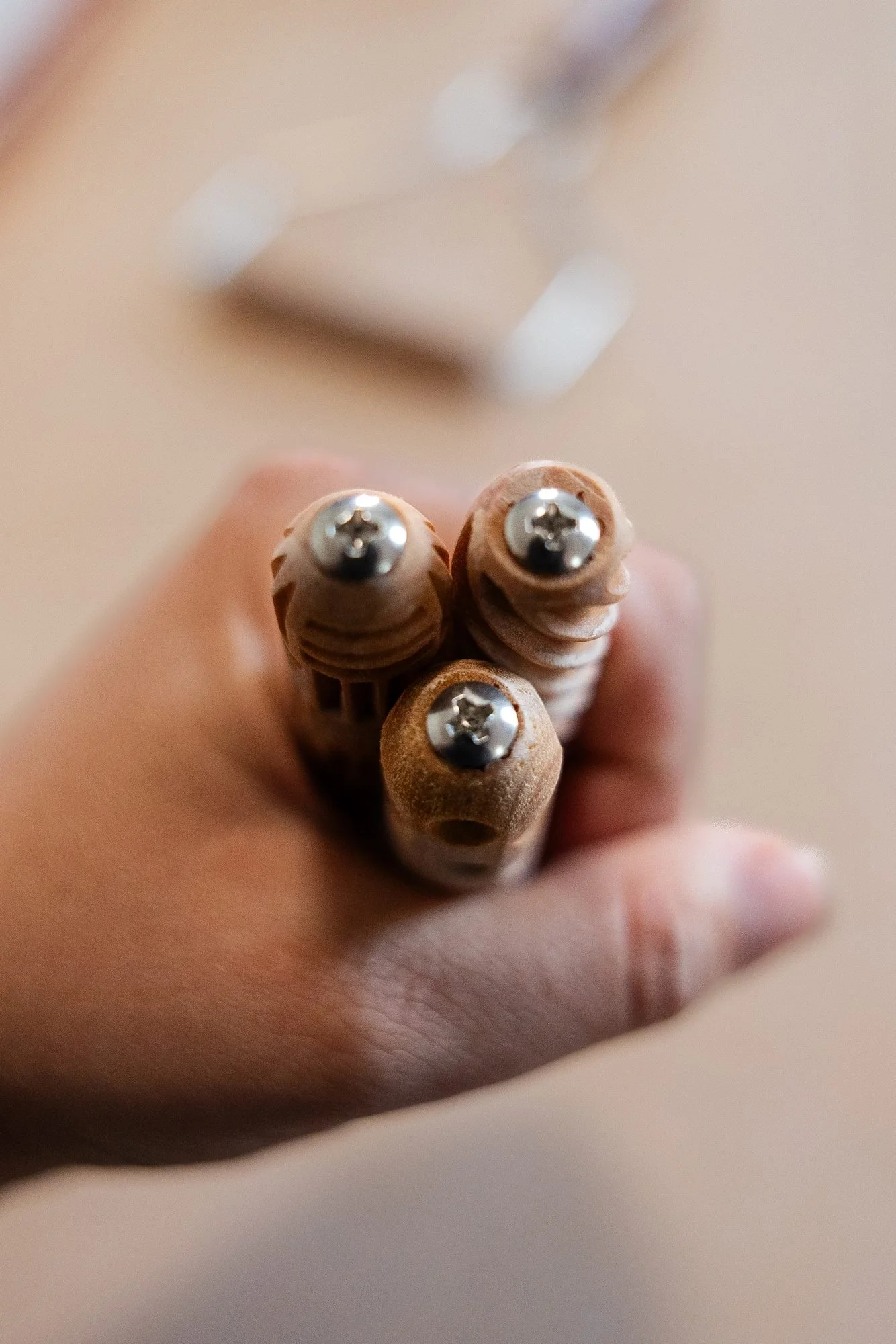 A hand holding three small wooden handled tools with round metal tips, fanned out toward the camera