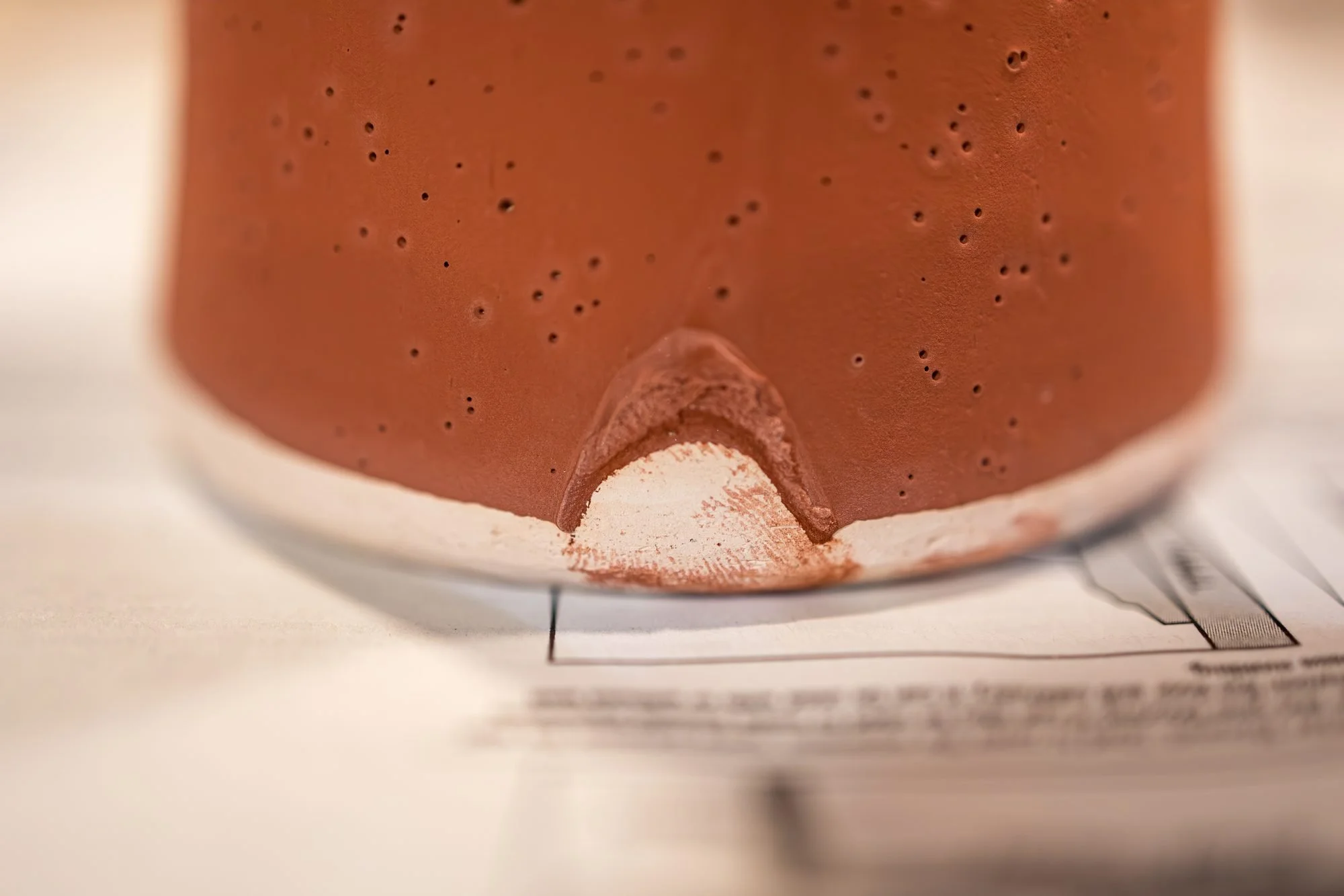 Close view of a pot in raw red glaze with a chipped patch near the base showing bare bisque underneath