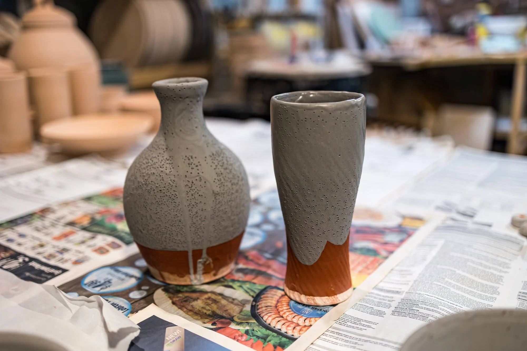 Two bottle shaped vases on newspaper, both coated in dull unfired glaze over red clay